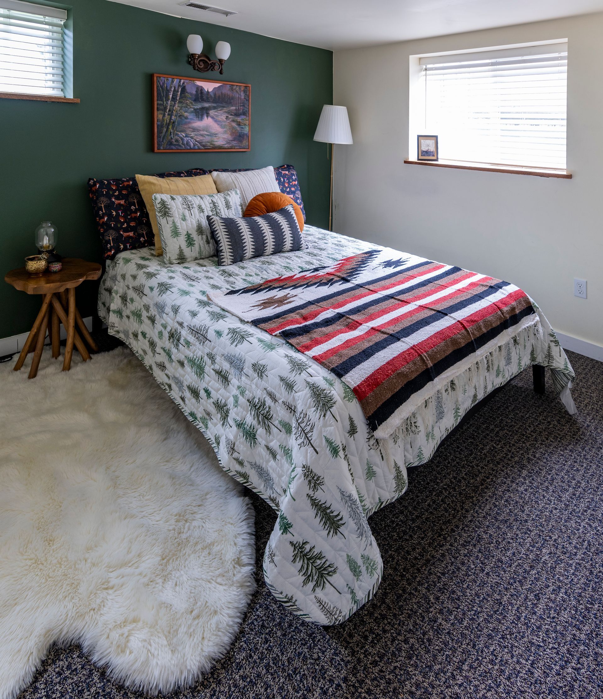 Cozy bedroom with patterned bedspread, dark green accent wall, windows, lamp, and fluffy white rug