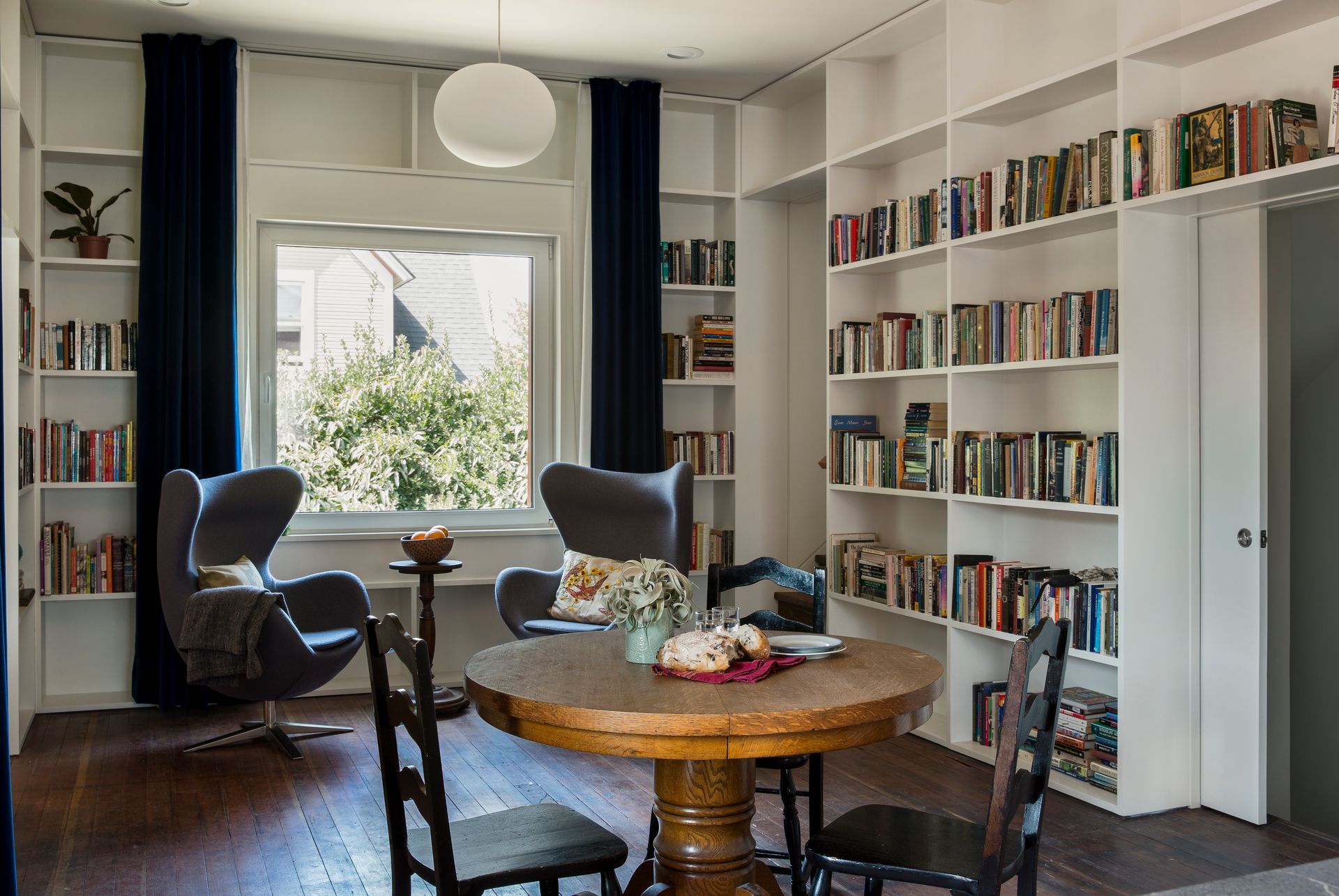 Bright dining room with built-in bookshelves, round wooden table, chairs, and a window seat.