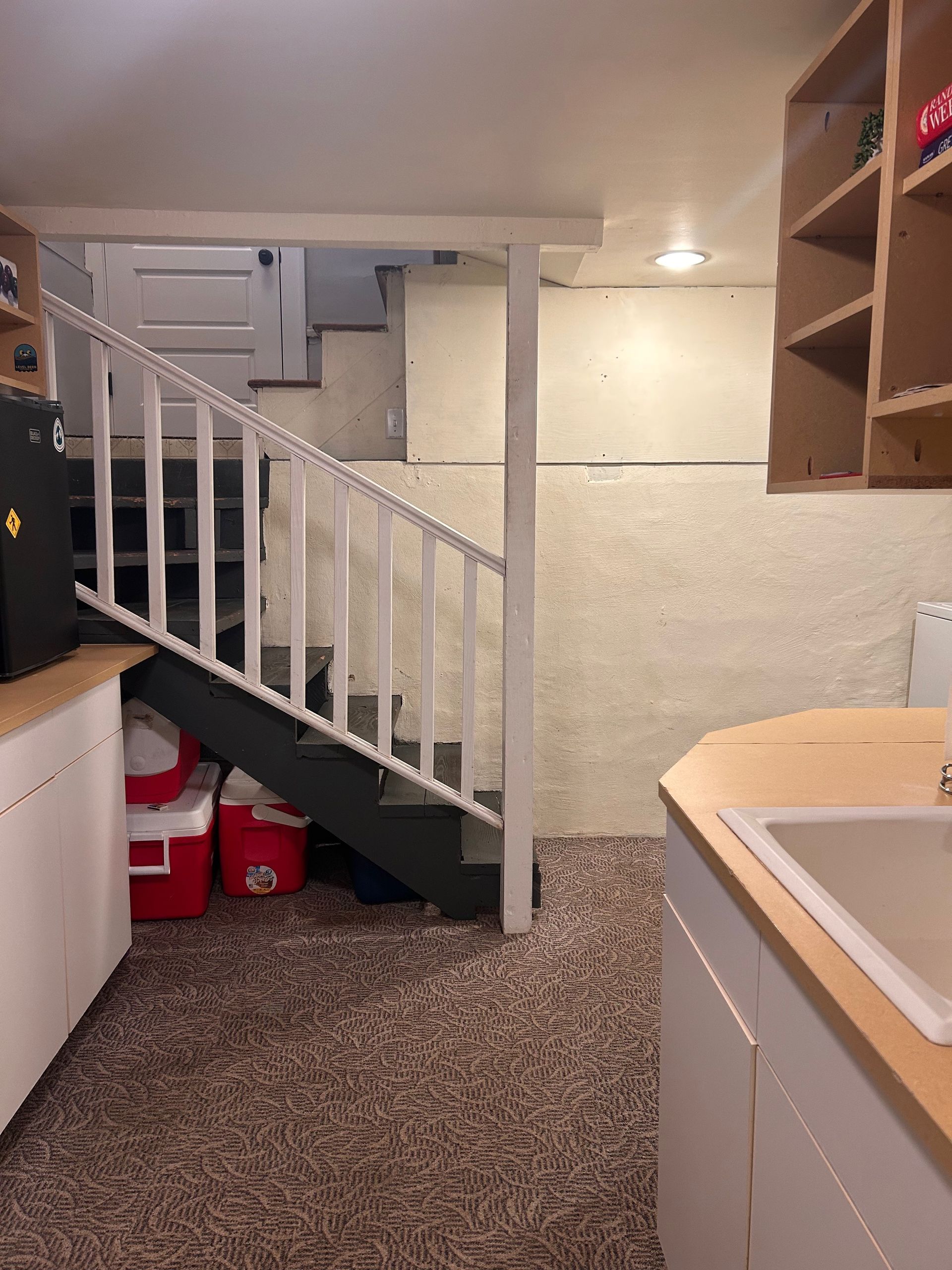 Basement laundry area with staircase, red buckets under stairs, and white cabinets by a sink