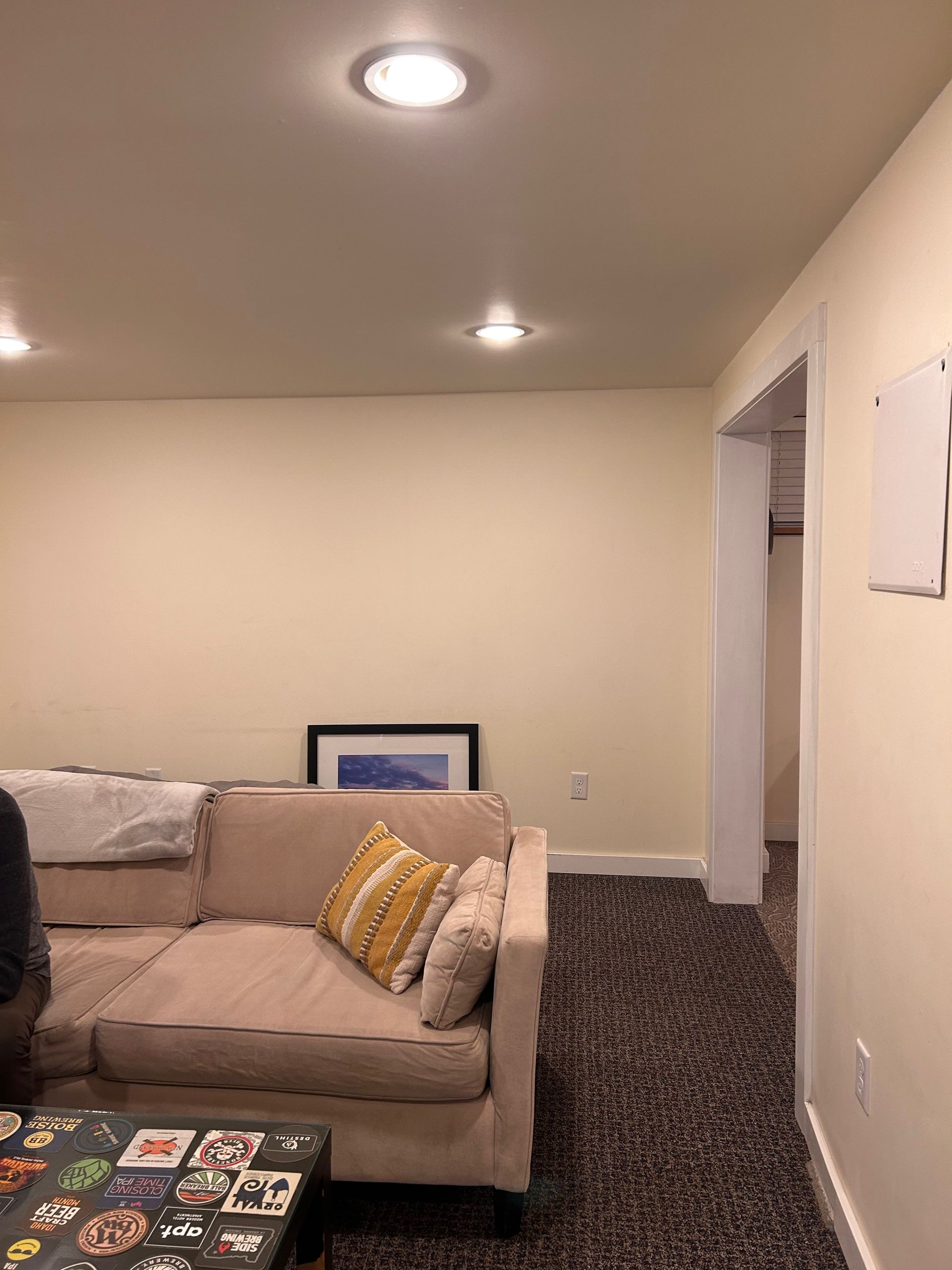 Basement living room with beige sectional, patterned rug, recessed lights, and white walls
