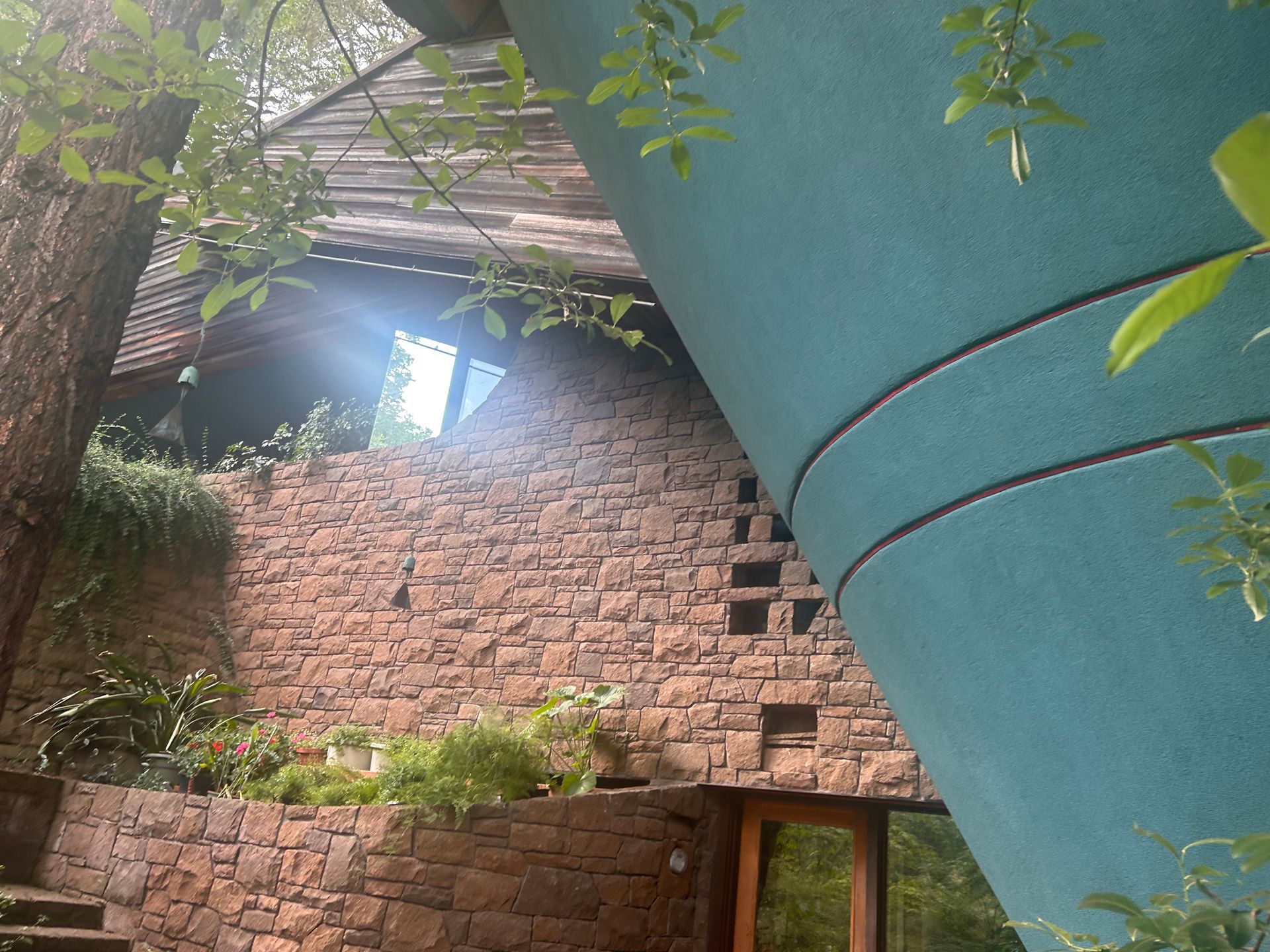 Red brick wall with a doorway, partly covered by a large turquoise tank and surrounded by green foliage.