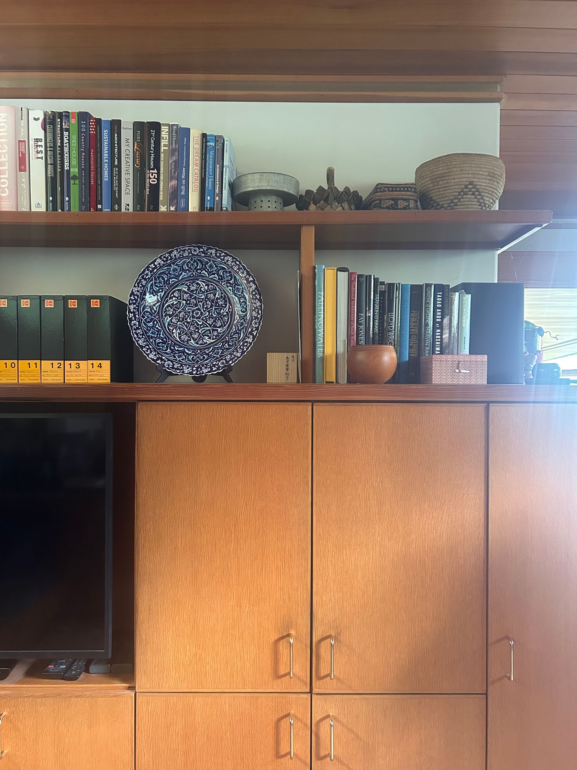 Wooden cabinet with books, decorative plates, and a TV in a living room