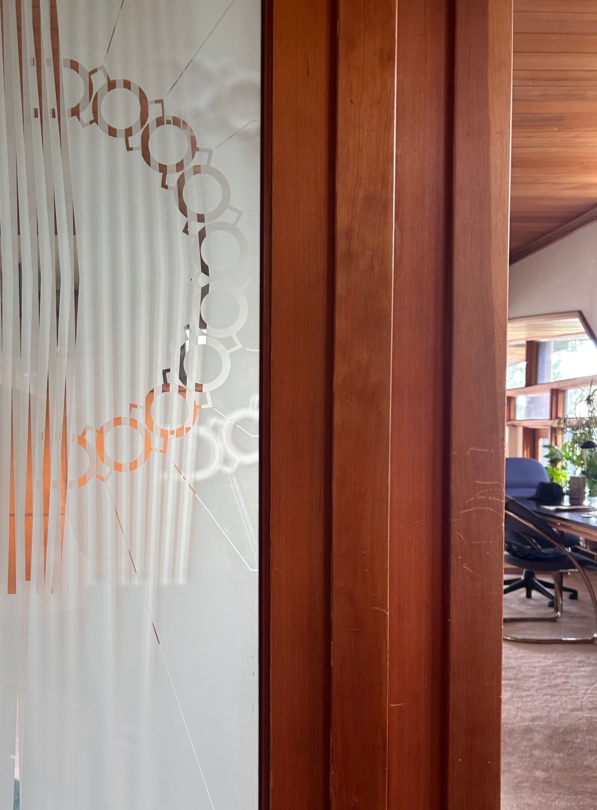 Wooden doorway beside frosted glass with circular design, opening to an outdoor patio and bookshelves beyond