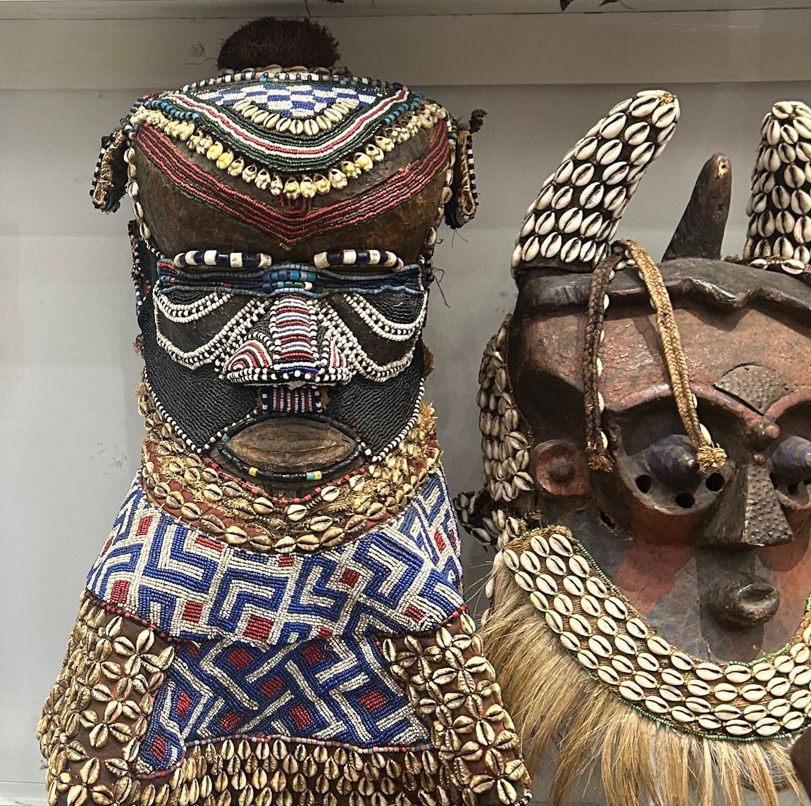Two ornate ceremonial masks with beaded and shell decorations on display shelf