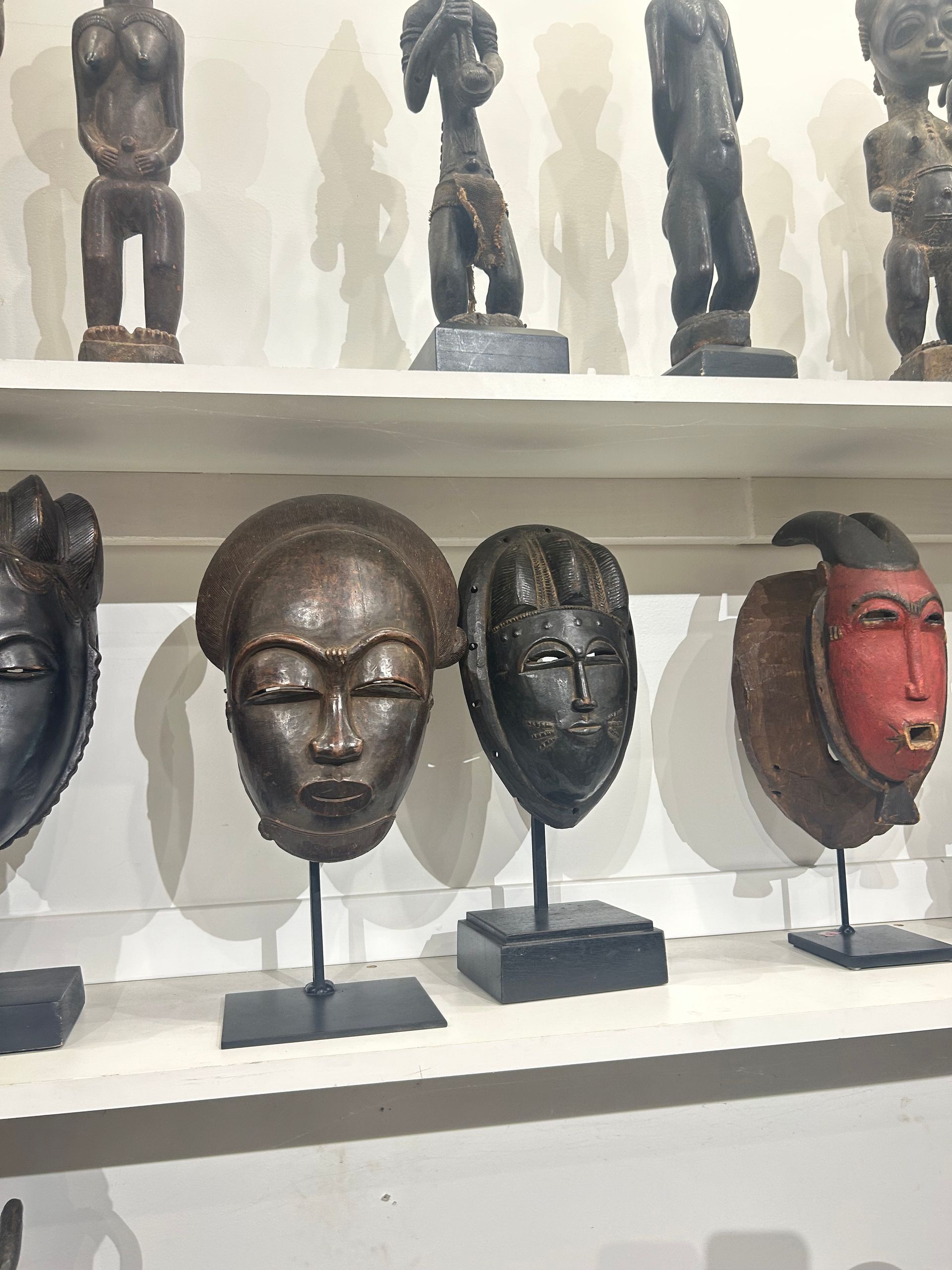 Shelves displaying carved masks and small figurines in a museum or gallery setting