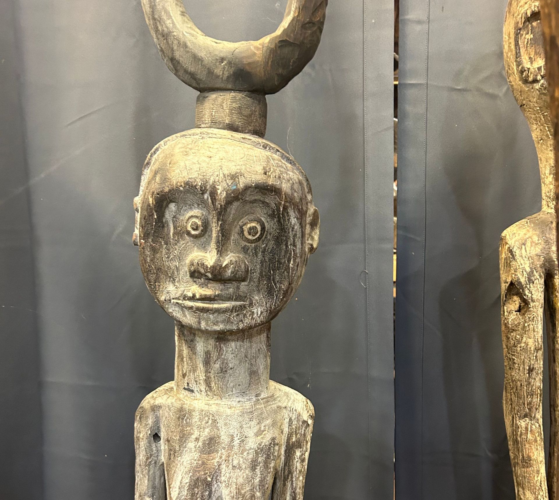 Weathered wooden tribal statue with a crescent shape above its head in a museum display.