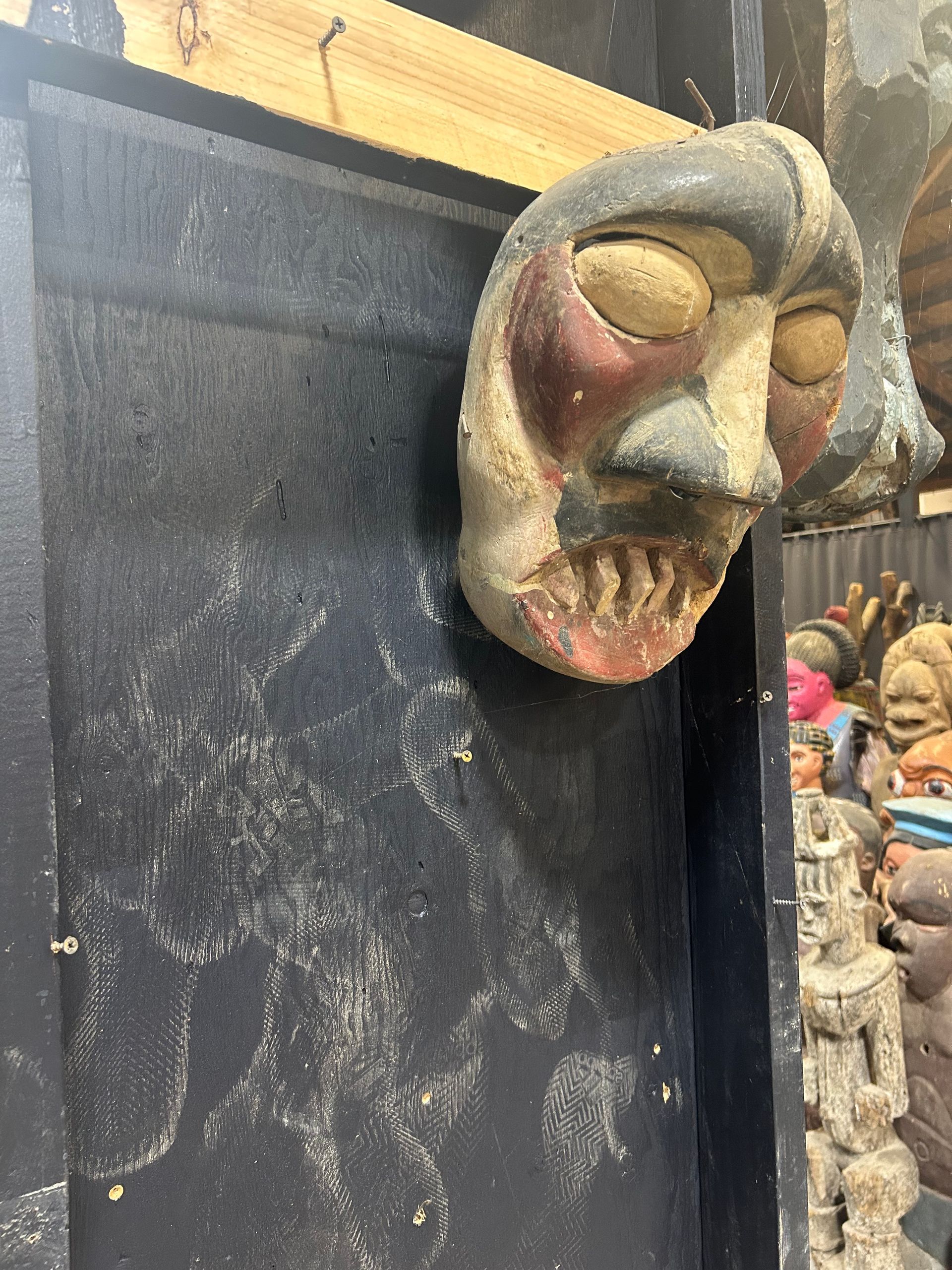 Weathered carved mask hanging on a black board in a rustic shop display