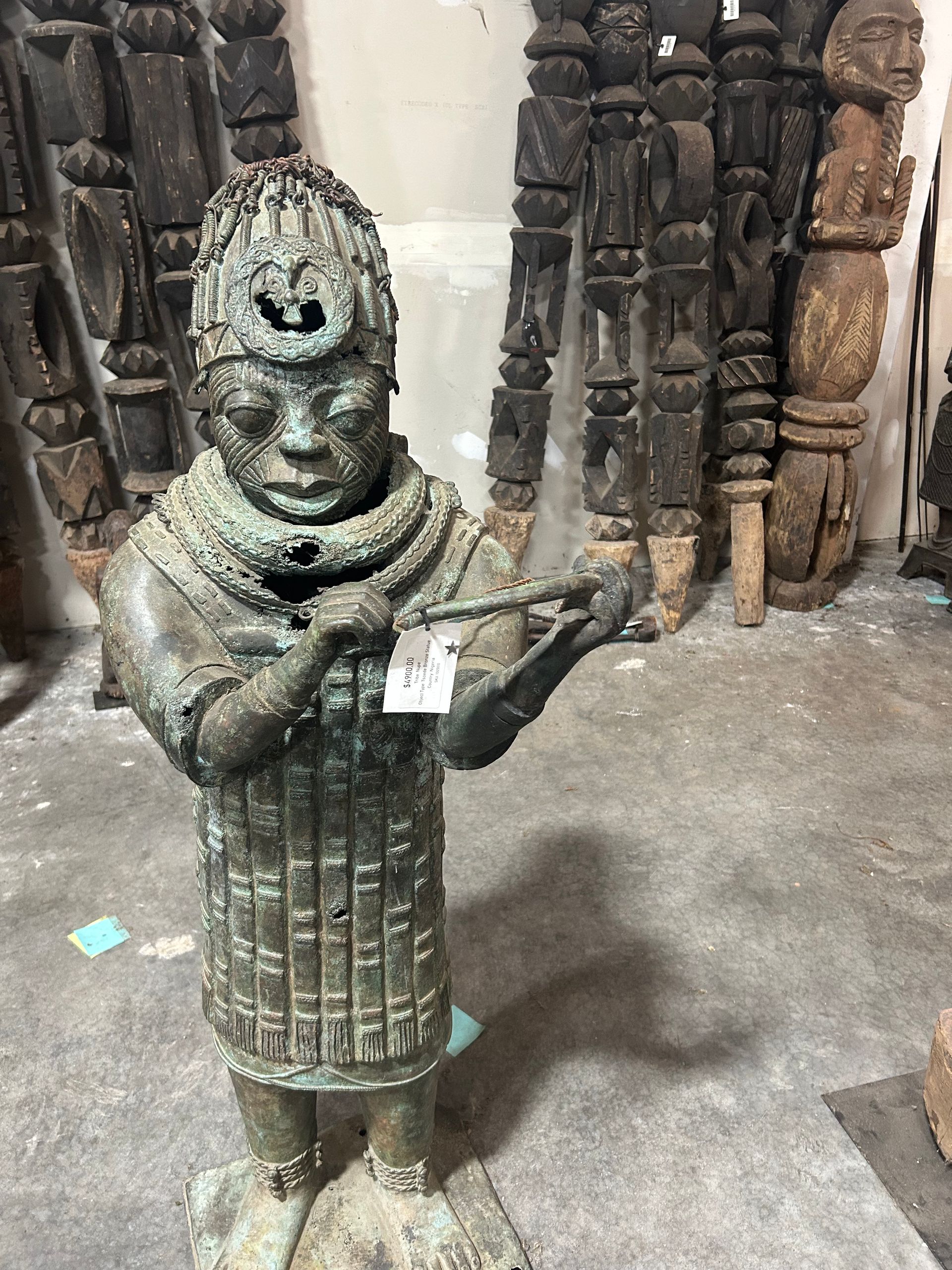 Stone statue of a robed figure in a museum display, holding an object, with carved pillars behind it