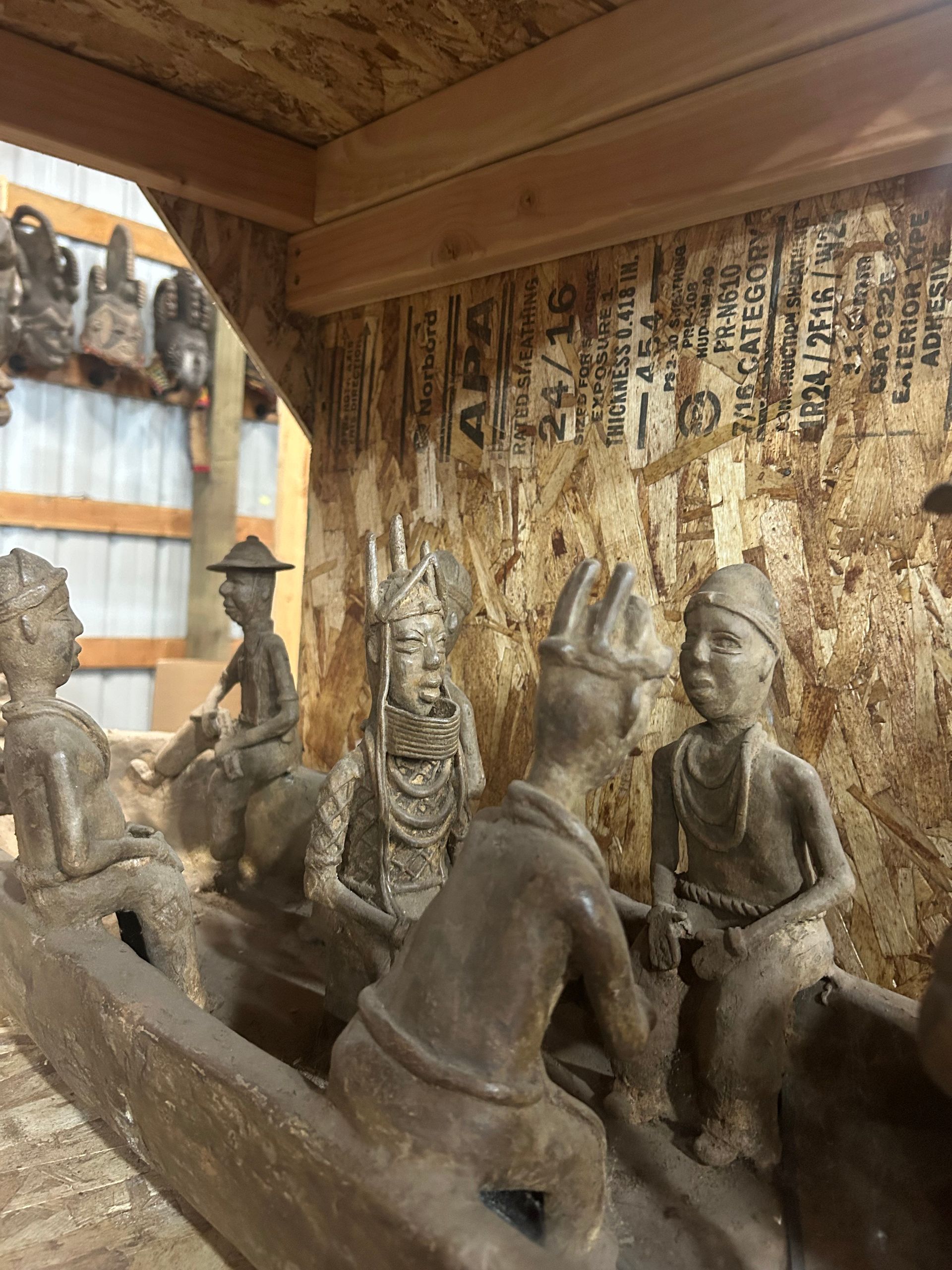Wooden sculptures of seated figures inside a rustic room with patterned walls and window light