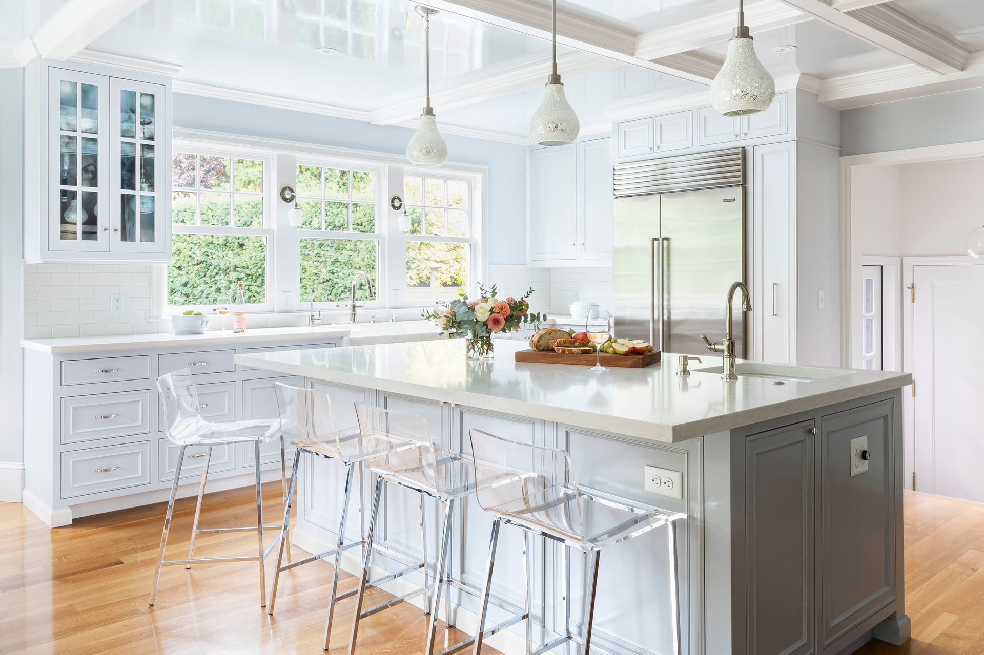 Bright white kitchen with large island, bar stools, pendant lights, and sunlit windows