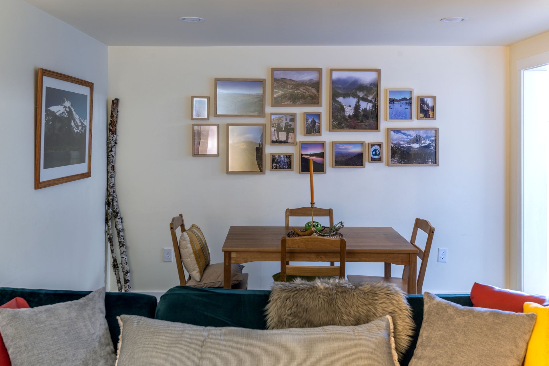 Cozy living room with couch in foreground, dining table, and a wall of framed art above the table.