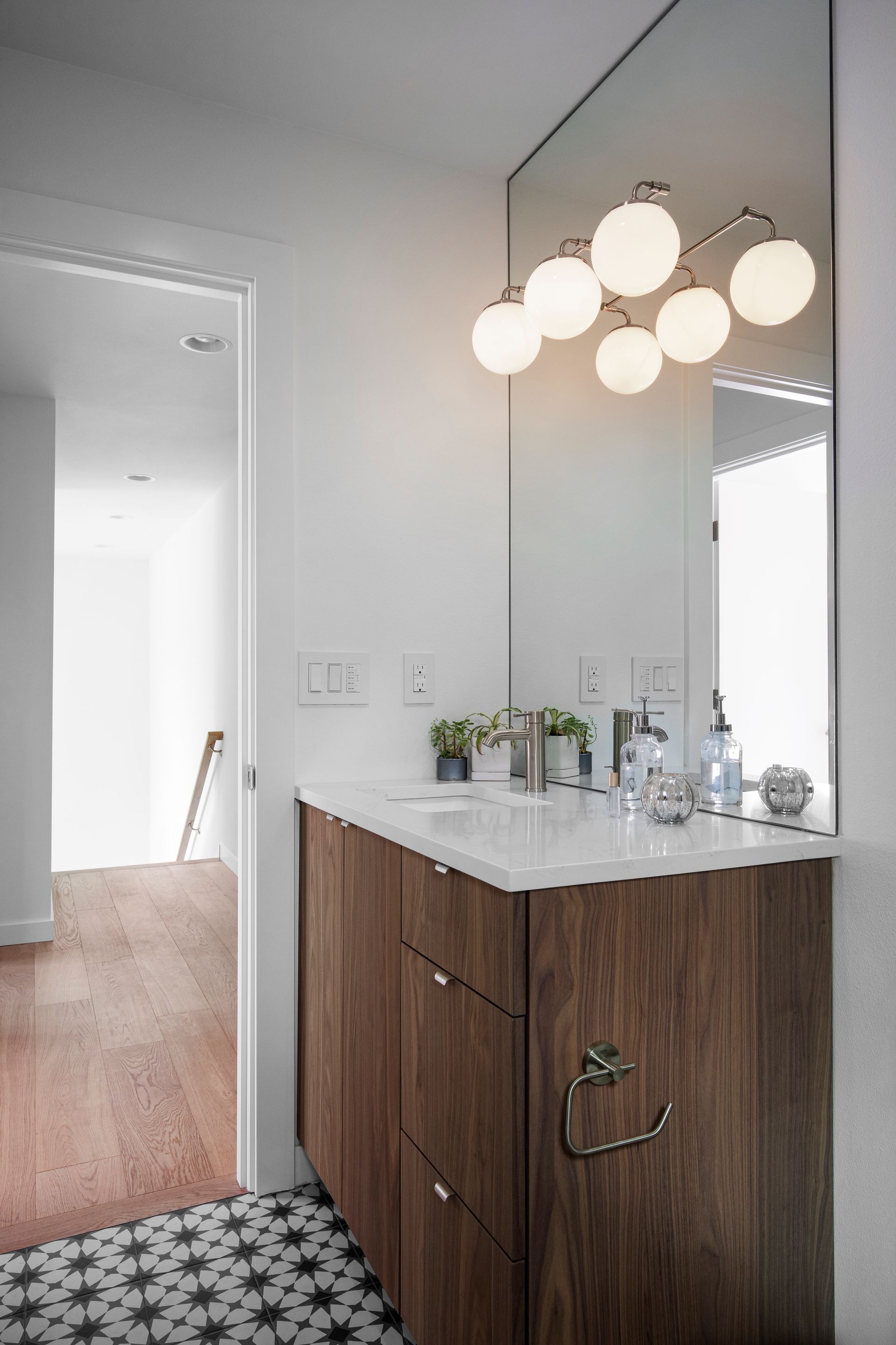 Modern bathroom vanity with wood cabinet, white sink countertop, round pendant lights, and large mirror