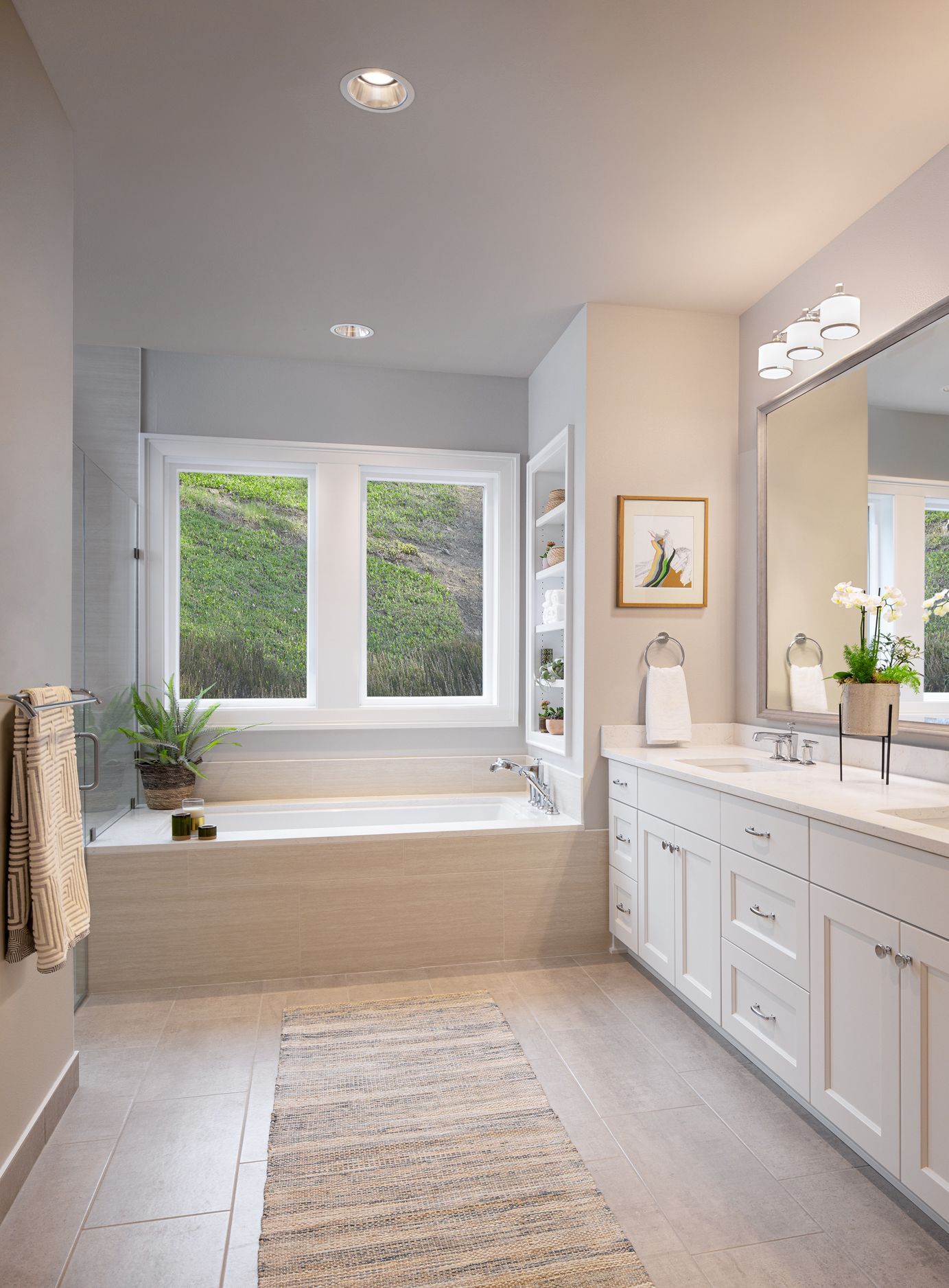Bright modern bathroom with vanity, large mirror, bathtub, and window seat by two windows