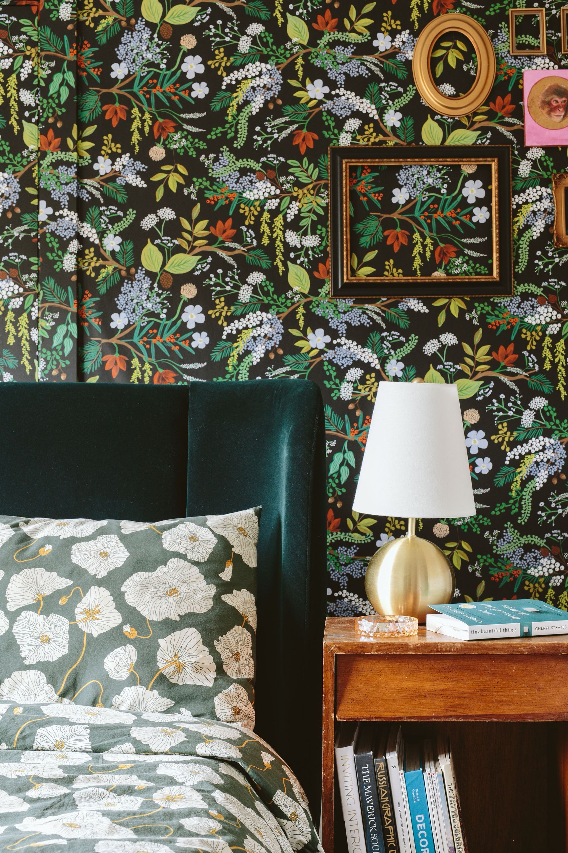 Bedroom with dark floral wallpaper, teal bed, patterned pillow, bedside lamp, and wooden nightstand