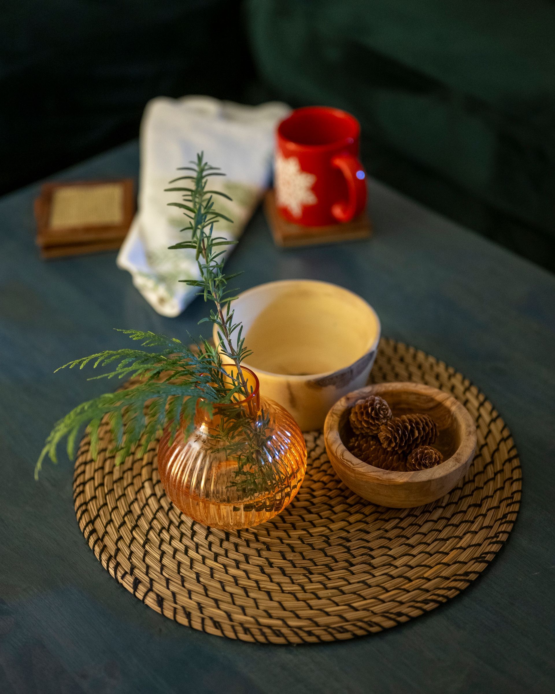A woven tray with a glass vase, ceramic cup, small bowl, and red candle on a table.