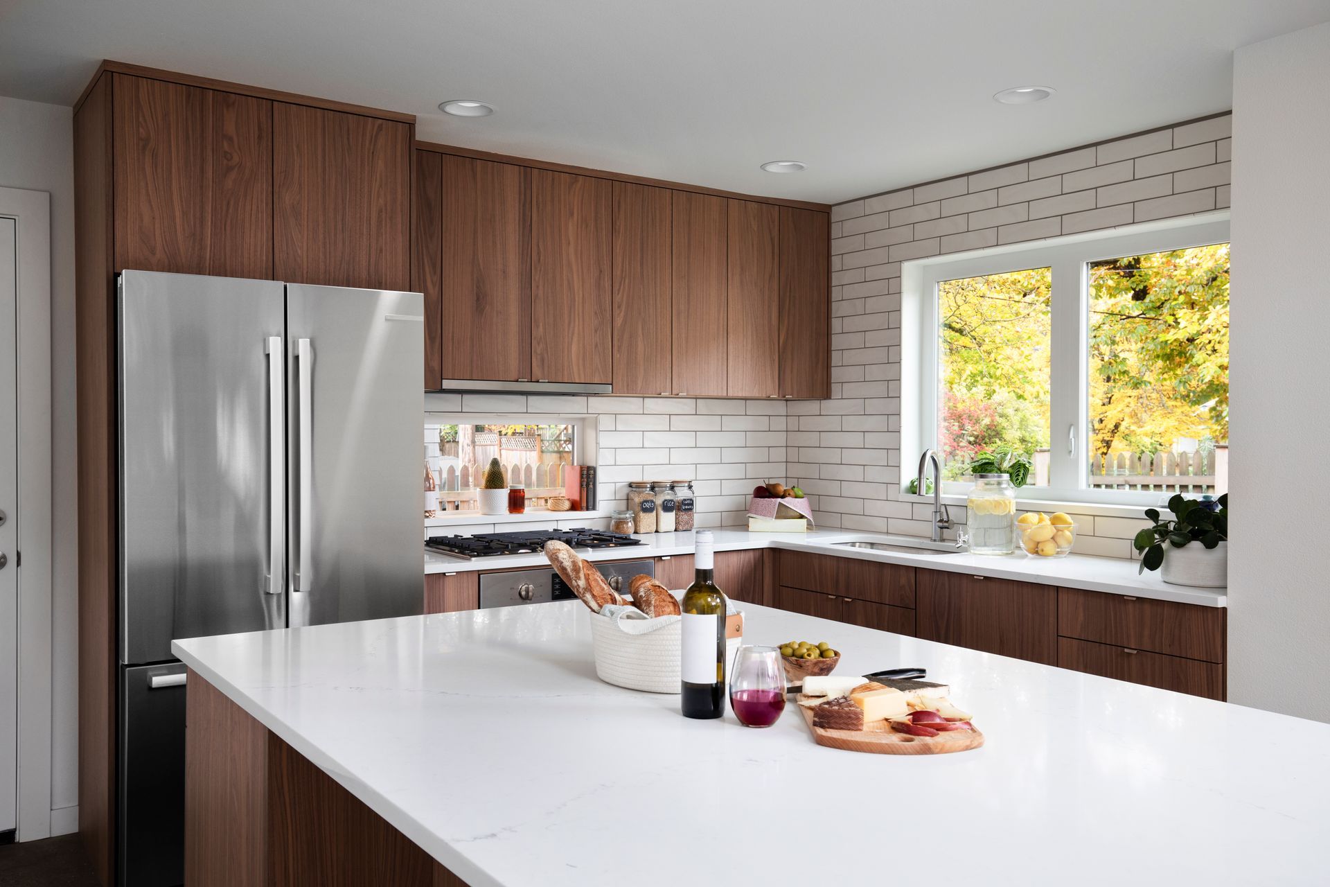 Modern kitchen with stainless steel fridge, wood cabinets, white island, and bright window view
