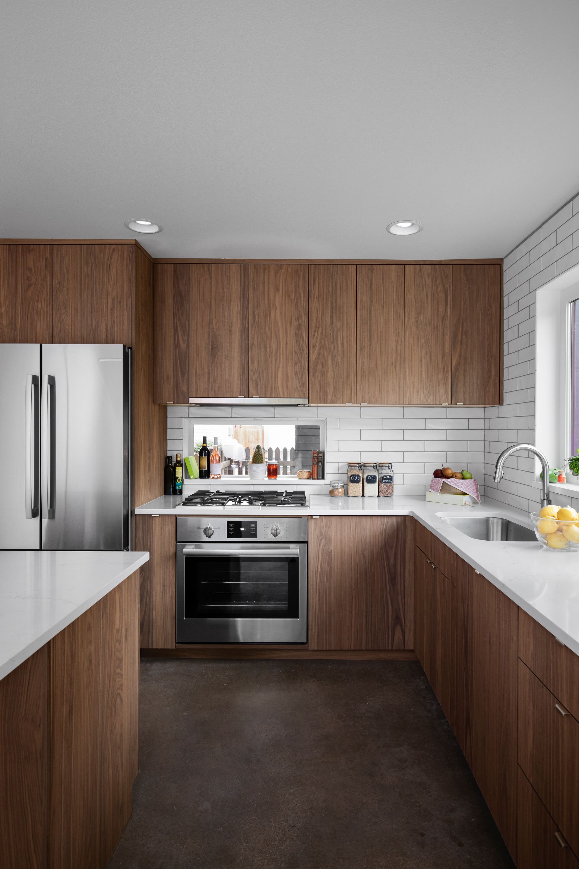 Modern kitchen with wood cabinets, white countertops, stainless steel appliances, and dark flooring.