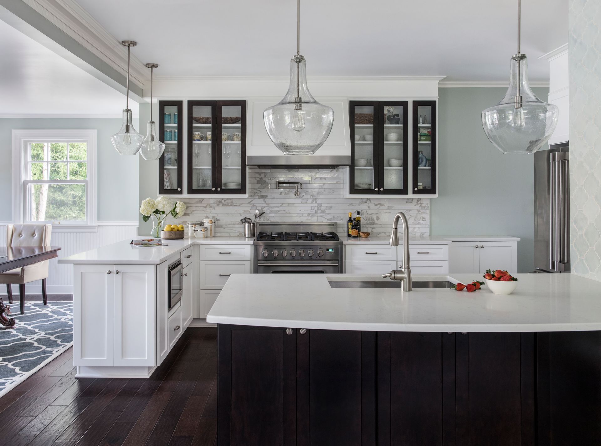 Bright modern kitchen with white island, dark cabinets, stainless stove, and pendant lights