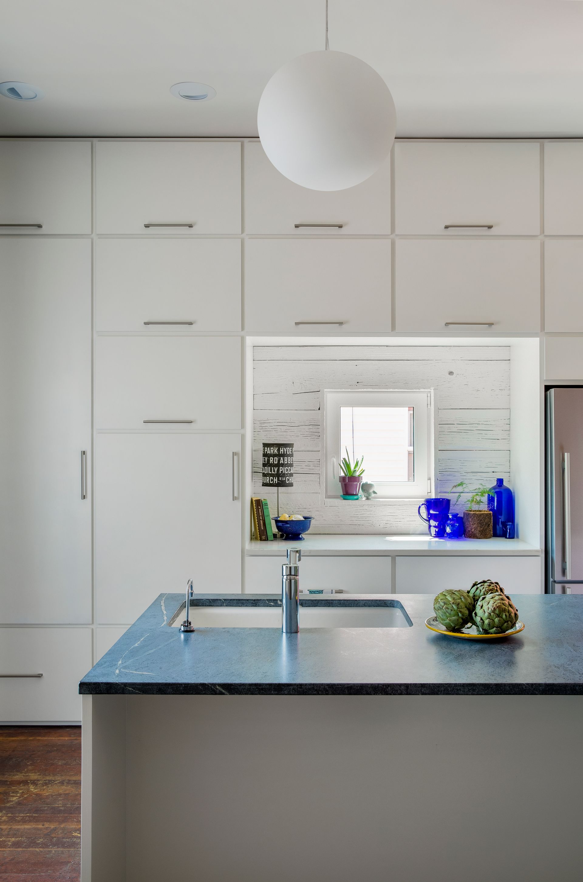 Modern white kitchen with blue island countertop, sink, and fruit on the counter