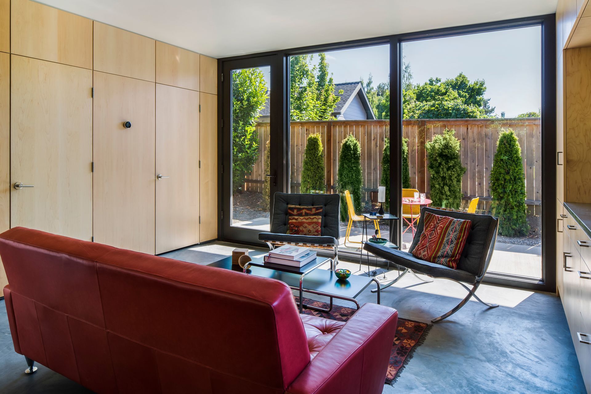Modern living room with red sofa, lounge chairs, and floor-to-ceiling windows overlooking a garden
