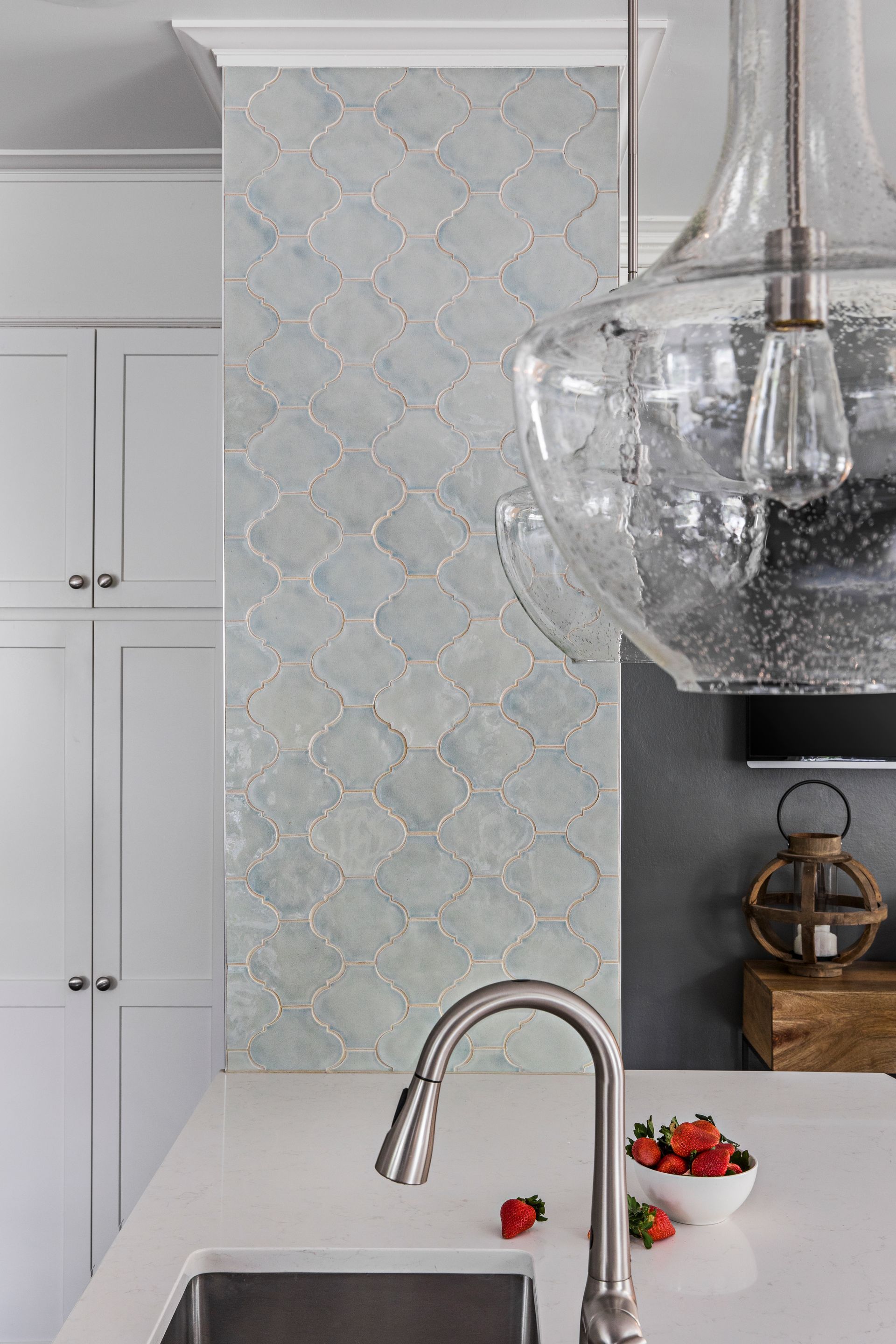 Bright kitchen with white cabinets, patterned backsplash, marble island, and hanging glass pendant light