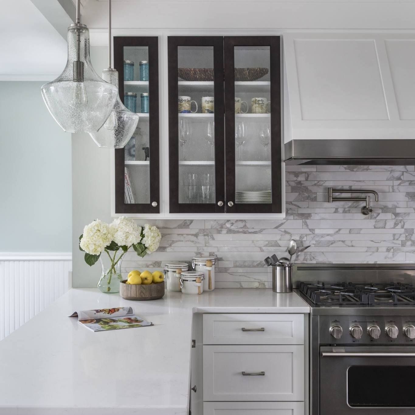 Bright white kitchen with dark cabinets, marble backsplash, glass pendant lights, and stainless steel stove