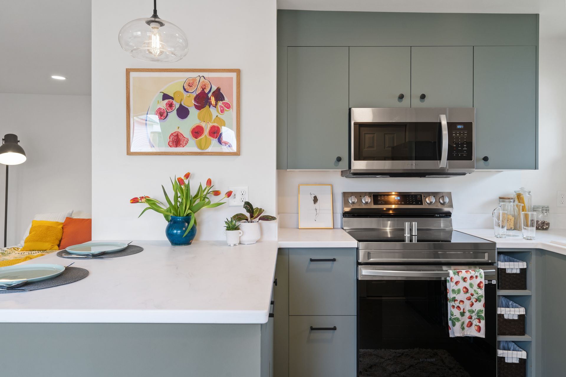 Modern kitchen with sage cabinets, white island, stainless appliances, and colorful decor.