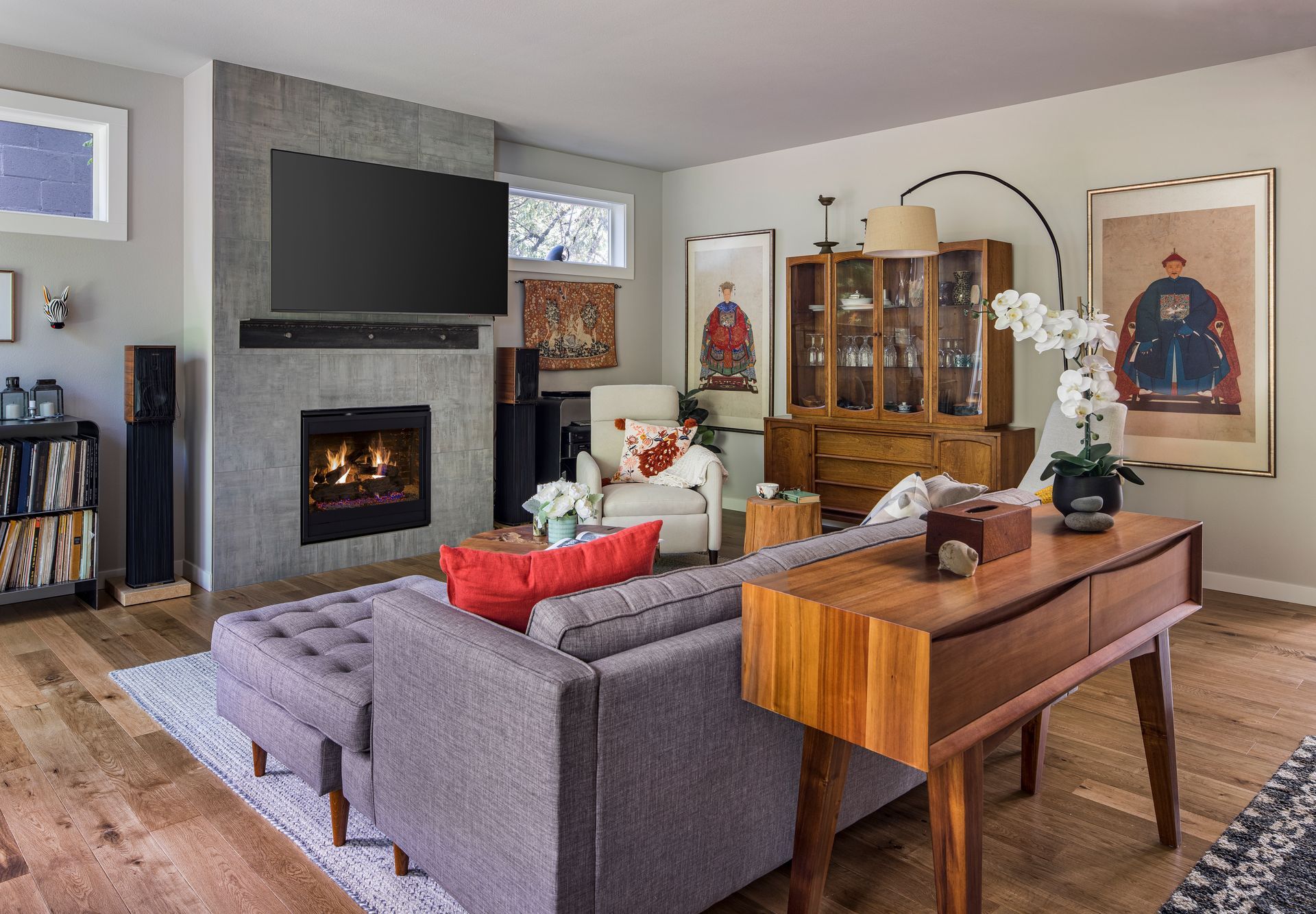 Cozy living room with a gray sofa, fireplace, wall-mounted TV, and a wooden dining table beside it