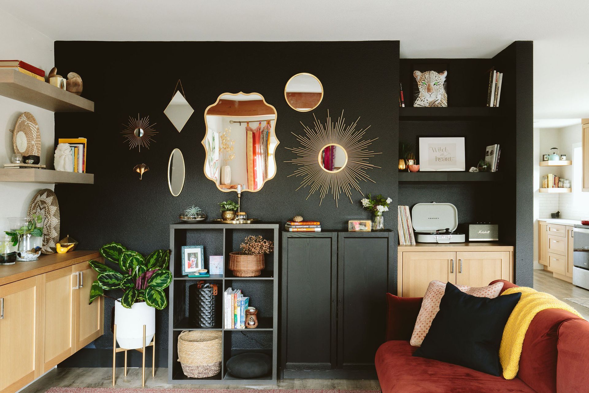 Modern living room with black accent wall, shelves, plants, and a red sofa with yellow throw blanket