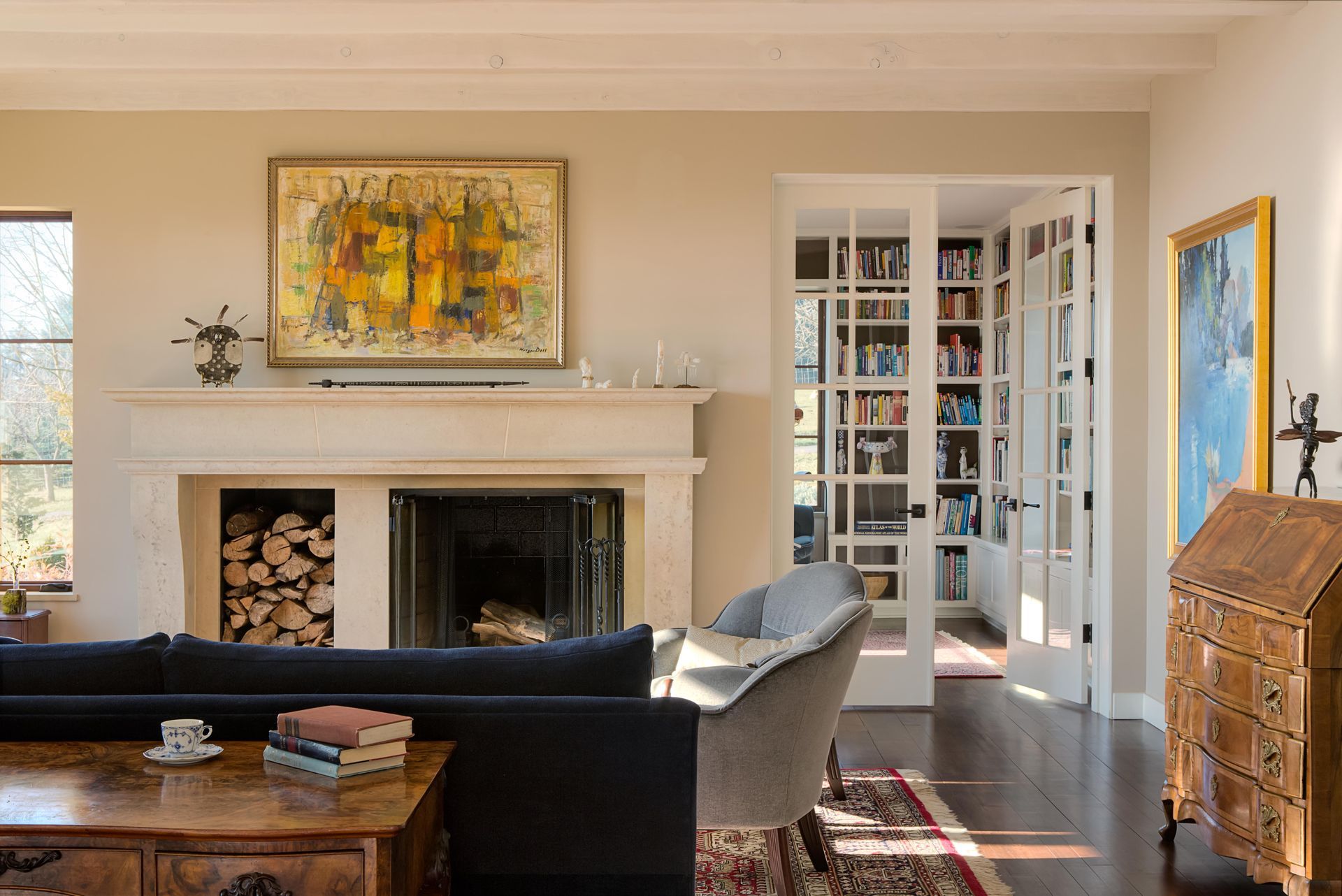 Bright living room with fireplace, sofa, artwork, and open glass doors to a sunlit hallway