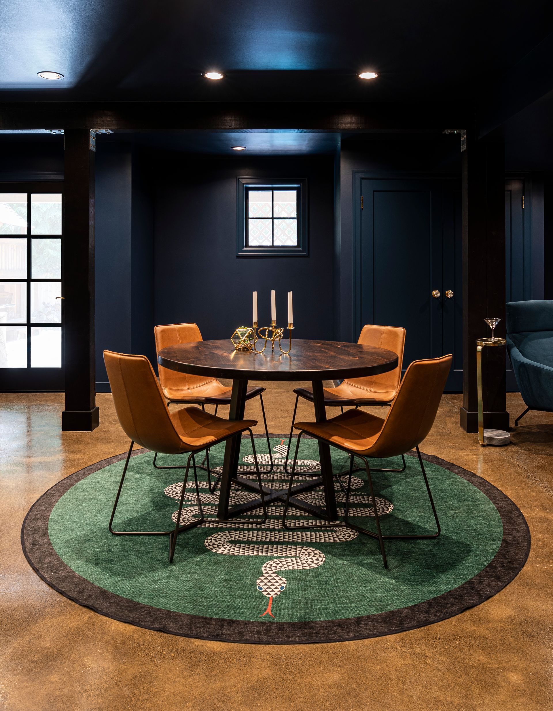 Modern dining room with a round wooden table, mustard chairs, and a green rug in a dark blue interior