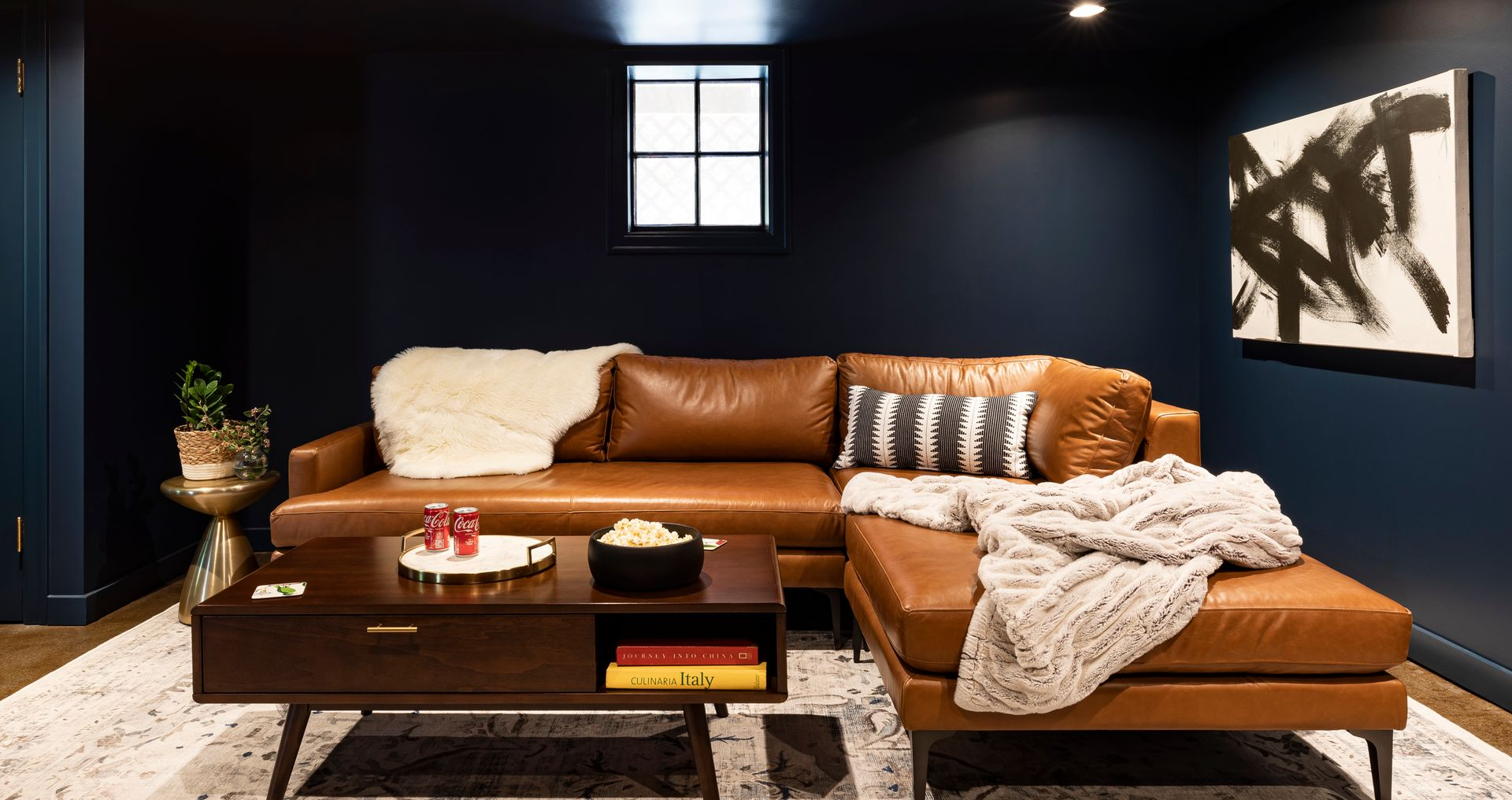 Modern living room with navy walls, tan sectional sofa, coffee table, rug, and abstract wall art