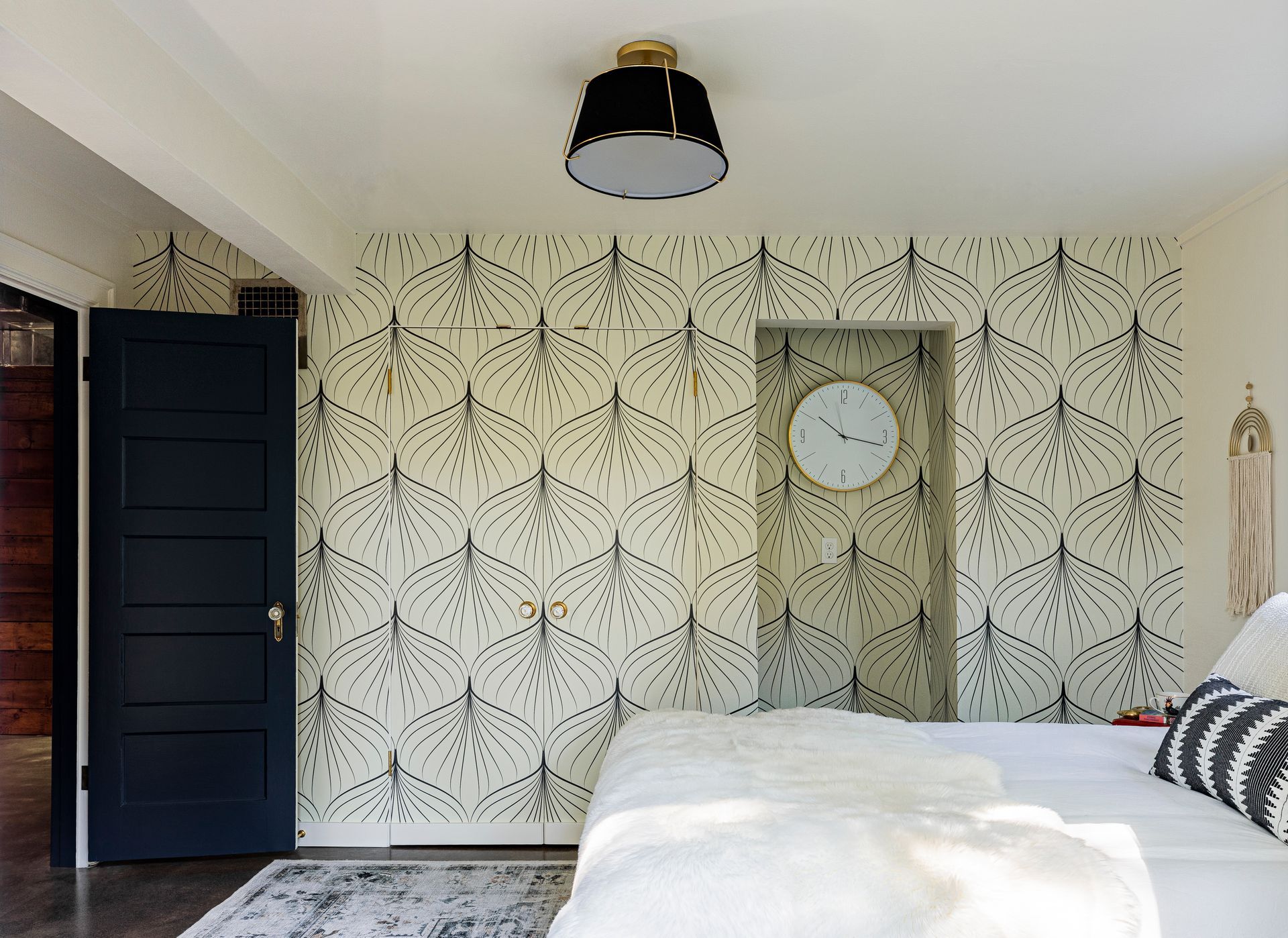 Bedroom with patterned wallpaper, black door, clock, and bed with white bedding