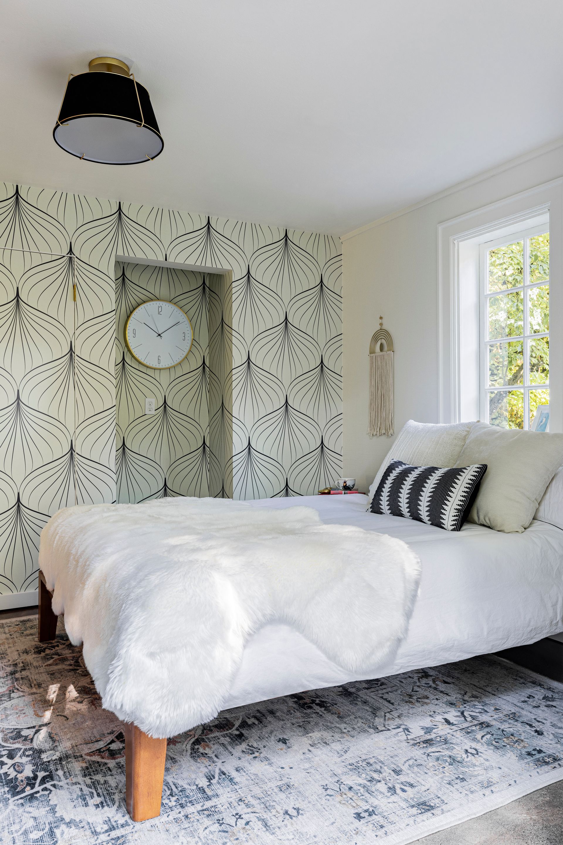 Bright bedroom with white bed, patterned wallpaper, large window, and black ceiling light.
