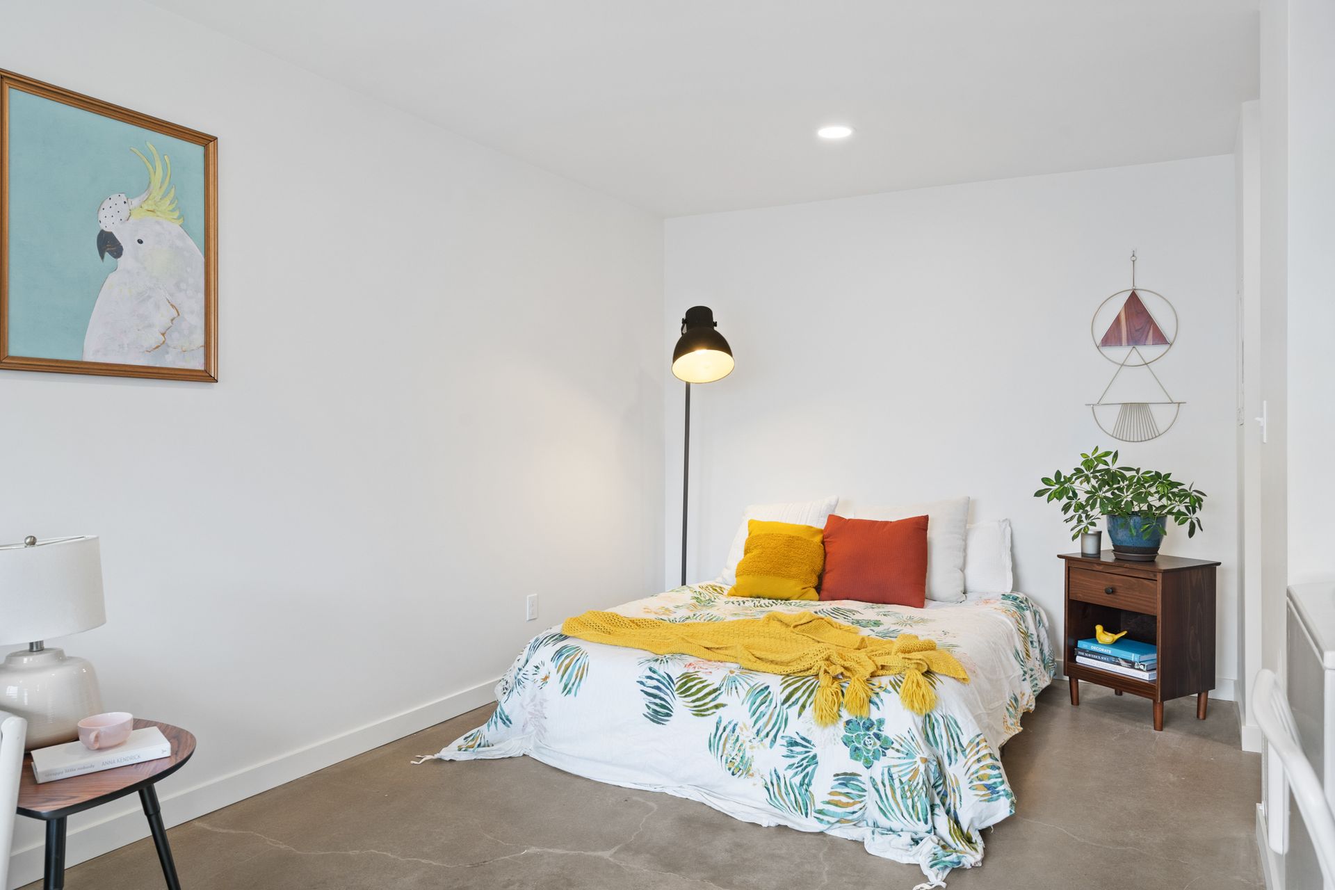 Bright bedroom with white walls, yellow bedding, floor lamp, and small plant on a side table