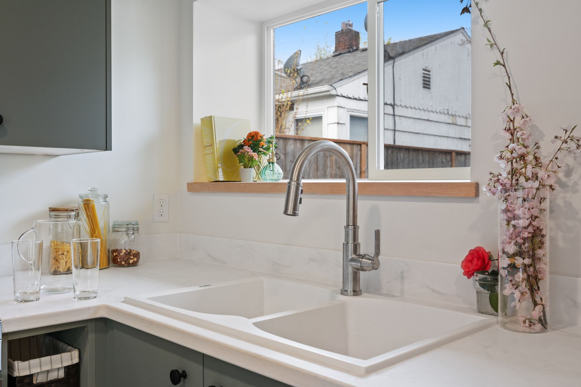 Bright kitchen sink under a window, with white countertop and flowers in a vase.