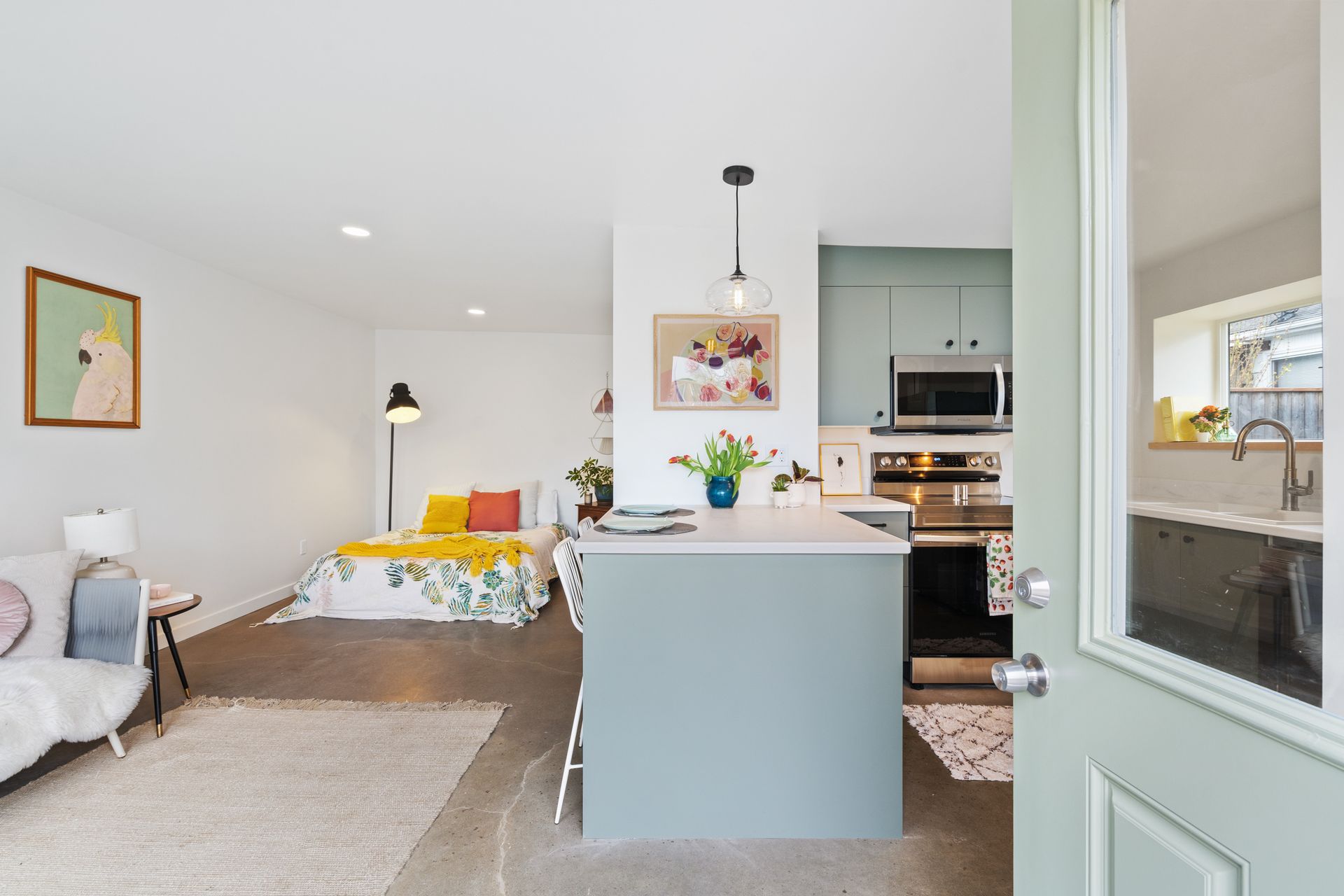 Bright, modern bedroom with bed, chair, and open kitchen area in soft mint and white tones