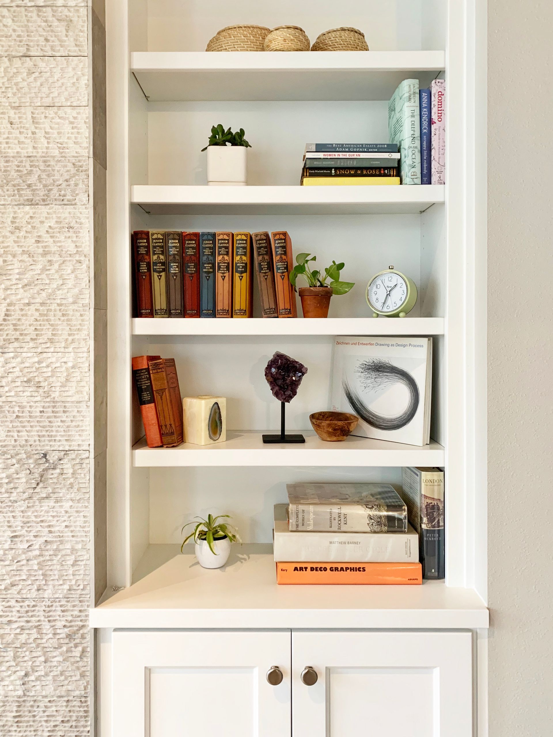 White built-in bookshelf with books, plants, decor, and a cabinet below