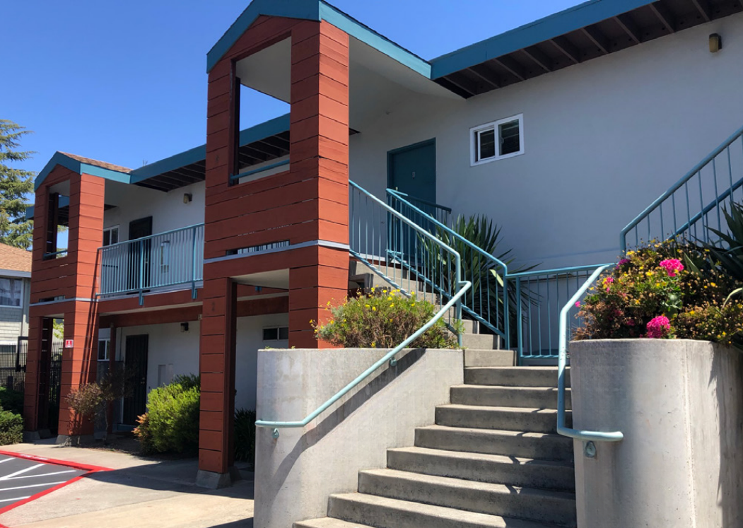 Exterior of a two-story apartment building with blue railings and concrete stairs.