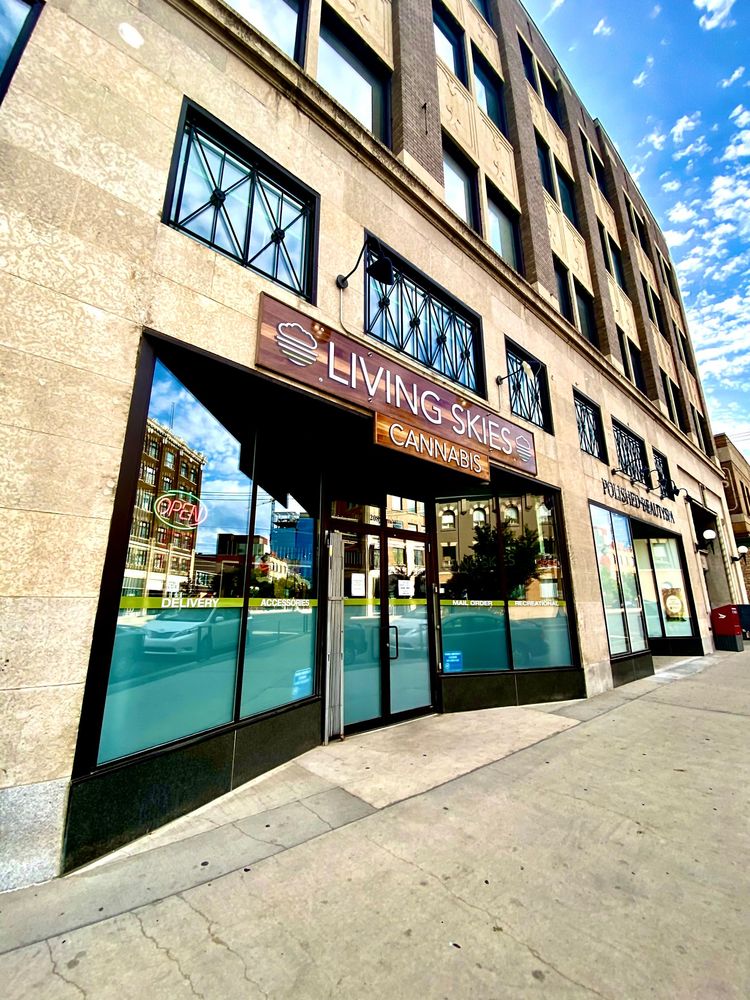 Street-level view of a brick building entrance with glass doors and blue storefront windows on a sunny sidewalk