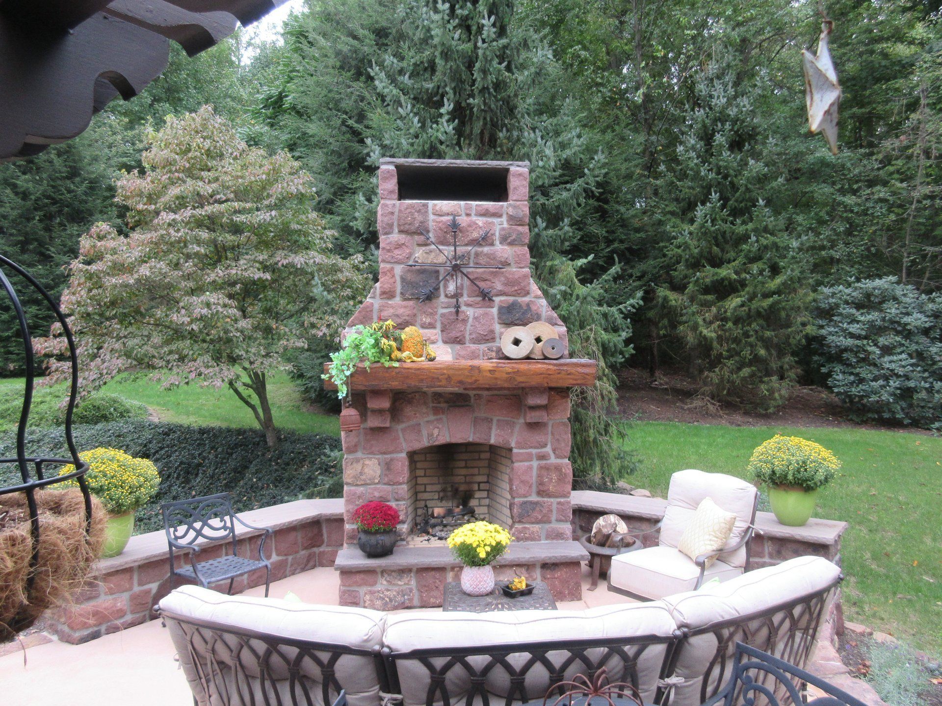 A brick fireplace in a backyard with a couch and chairs