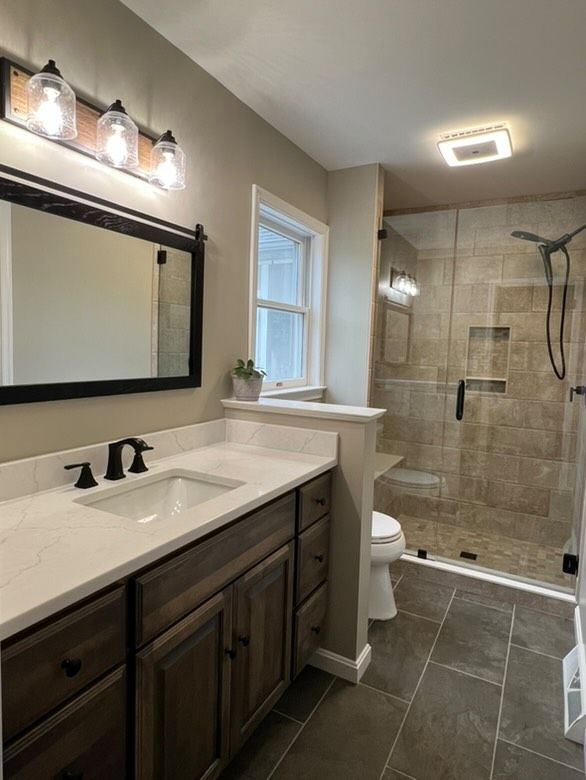 A bathroom with a sink , toilet , shower and mirror.
