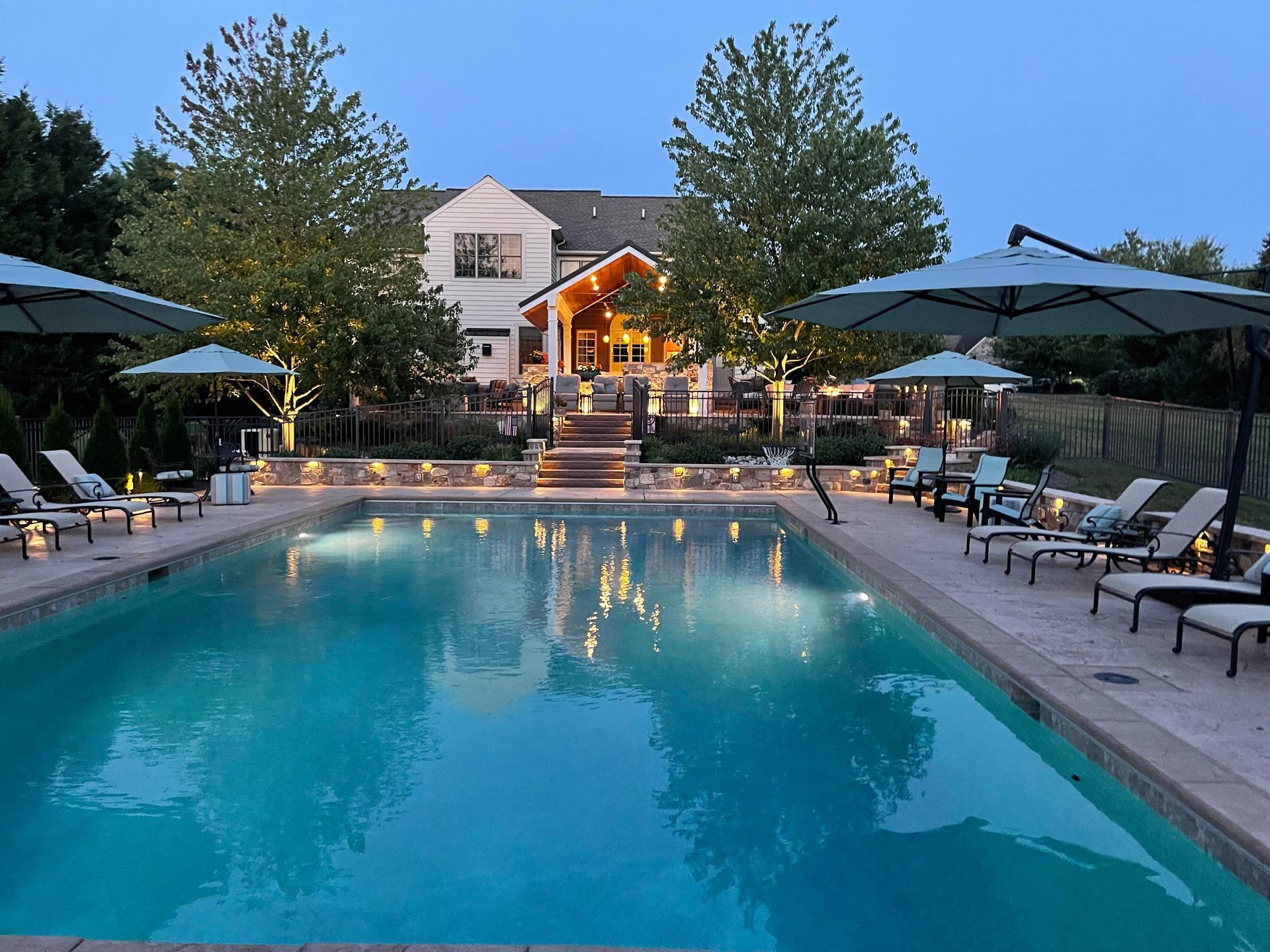 A large swimming pool is surrounded by chairs and umbrellas in front of a house.