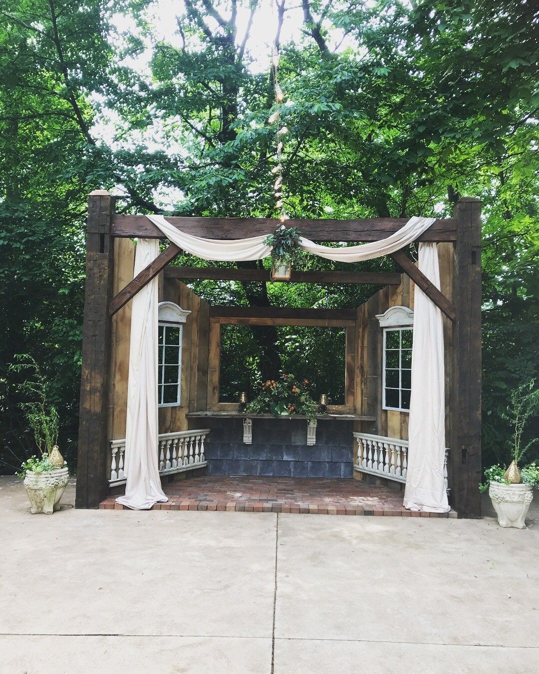 A wooden structure with white curtains is surrounded by trees.