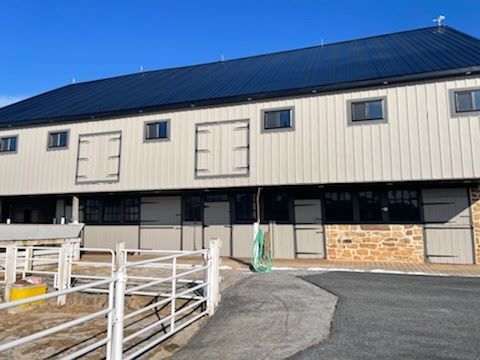 A large barn with a black roof and a fence around it