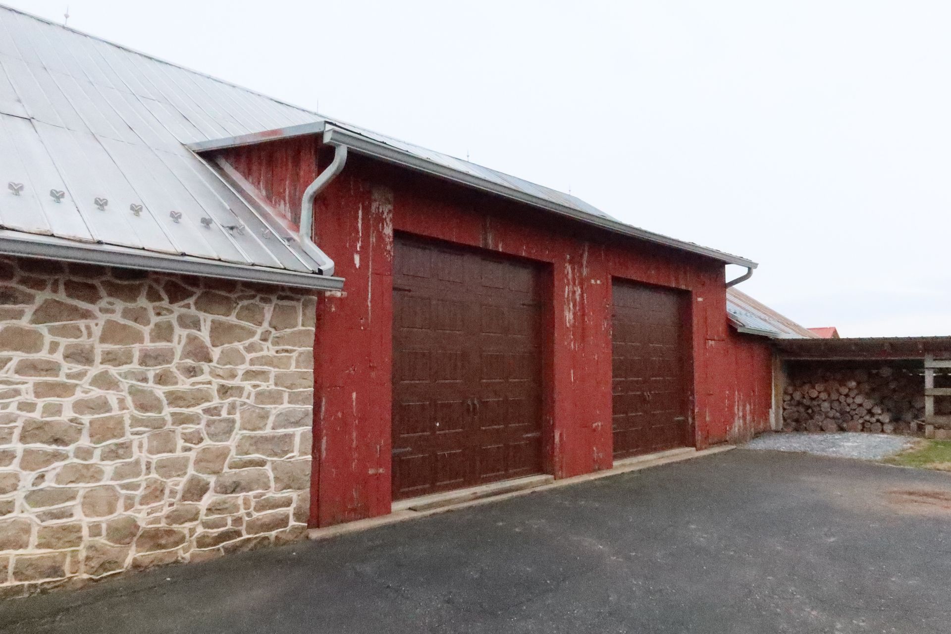 A red barn with three garage doors and a stone wall.