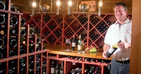 A man is standing in a wine cellar holding a bottle of wine