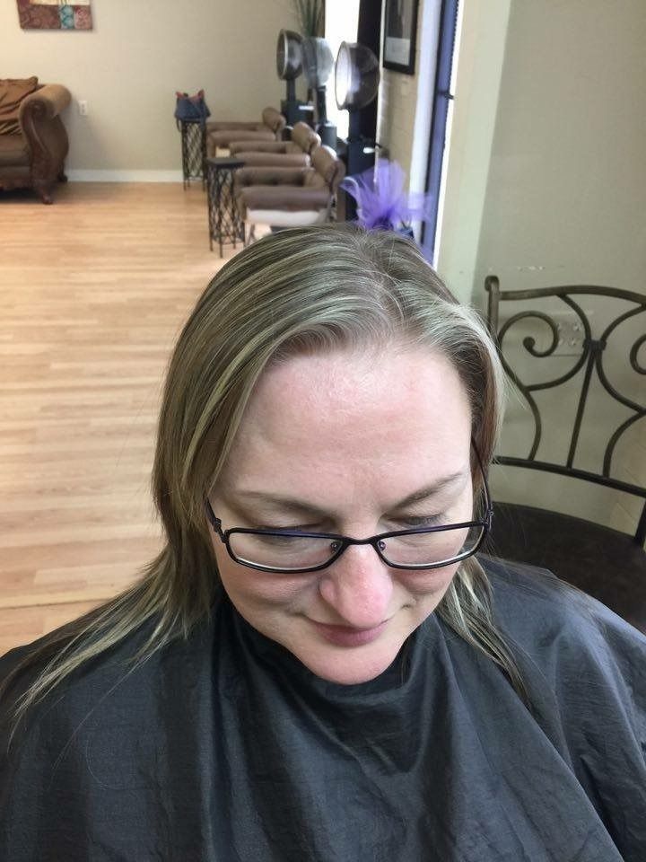 Person with glasses looking down in a room with wooden floors and chairs in the background