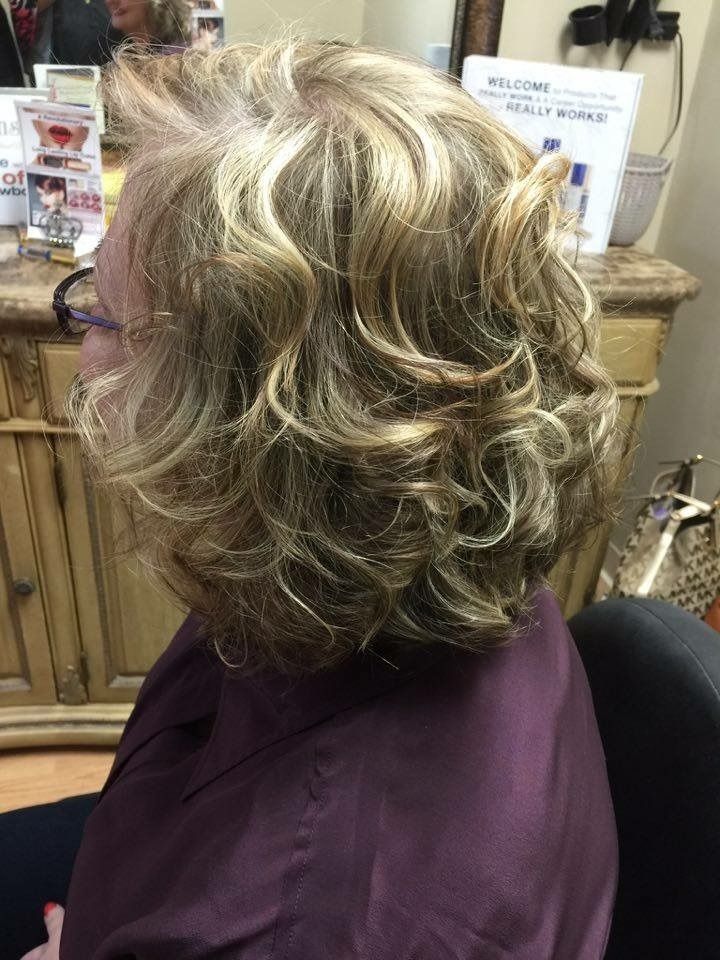 Short layered blonde and brown haircut with curls, shown from the side in a salon chair