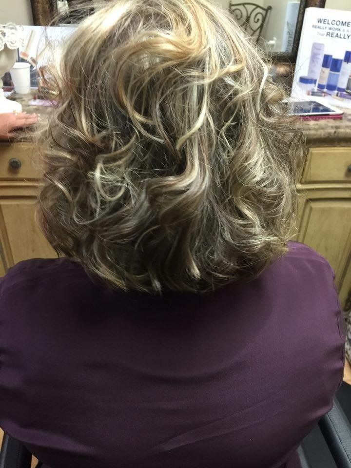 Back view of a person with highlighted, curly shoulder-length hair in a salon chair.
